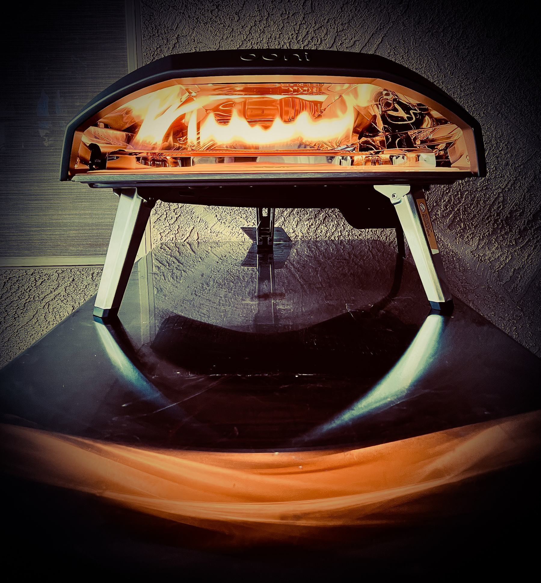 Auto-generated description: A pizza oven emits a fiery glow on a reflective surface, creating a dramatic lighting effect.