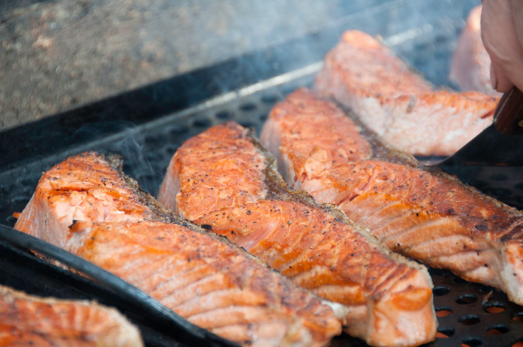 Auto-generated description: Several pieces of seasoned salmon are being grilled.