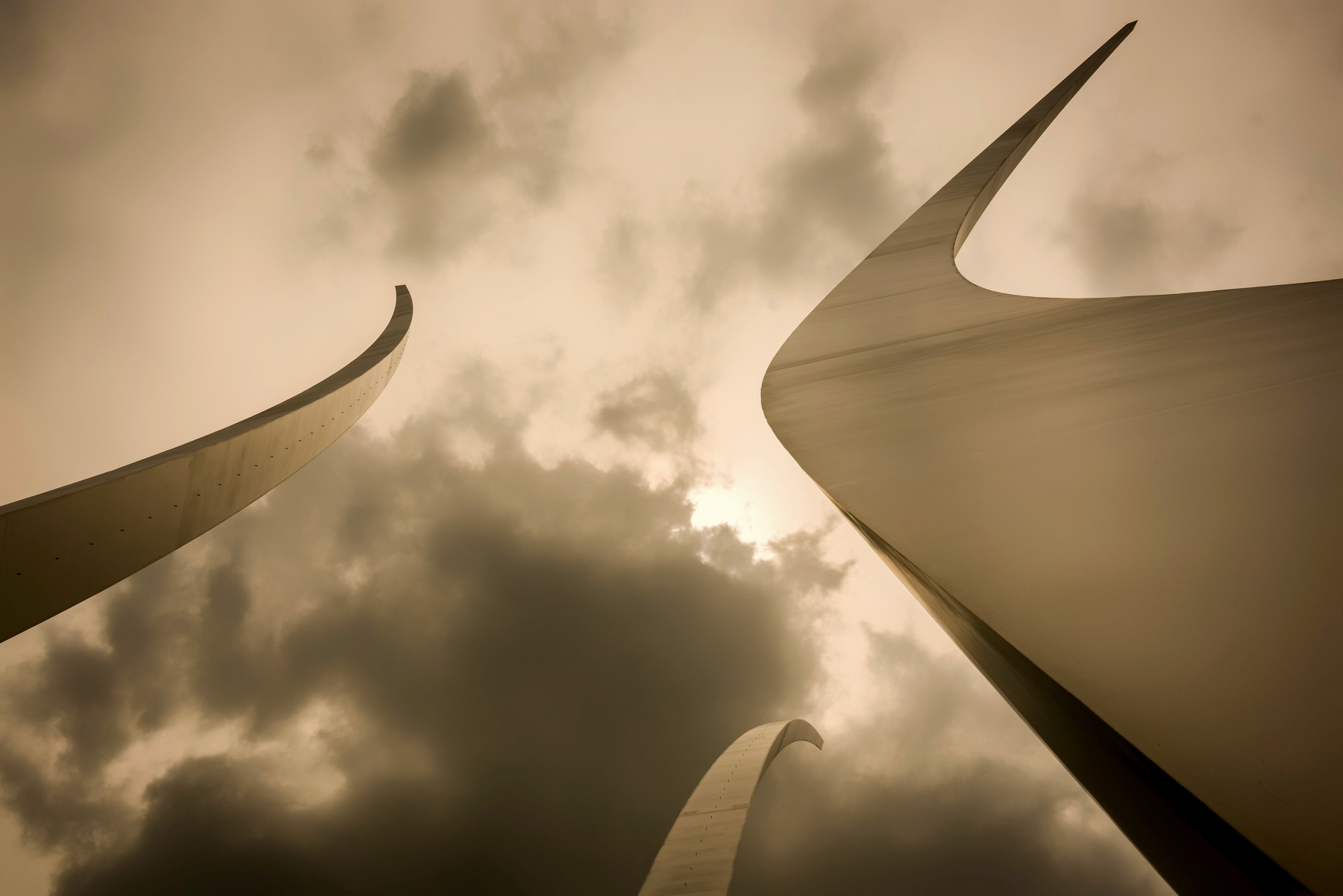 Auto-generated description: Tall, curved architectural structures reach up toward a cloudy, moody sky.