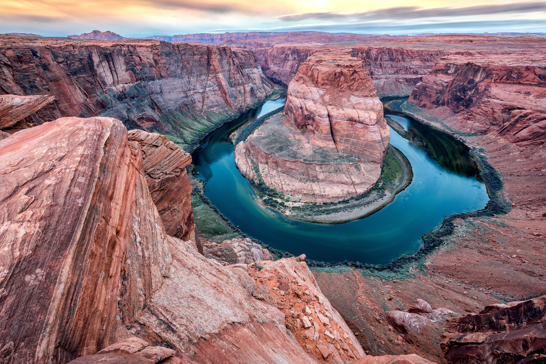 Auto-generated description: A river beautifully curves around a rock formation in a dramatic desert landscape at sunset.