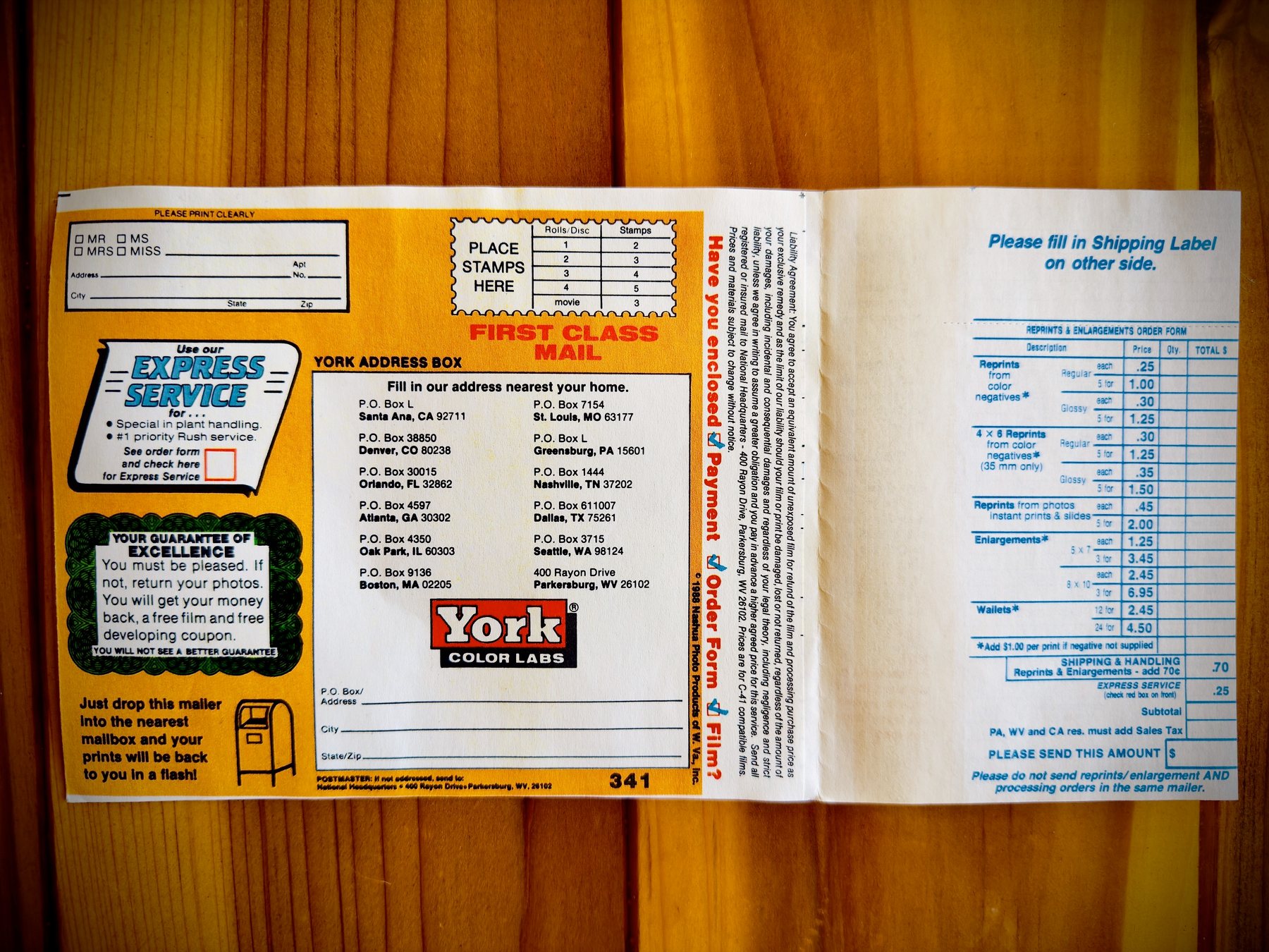 Auto-generated description: A mail-in photo development envelope for York Color Labs with mailing instructions, address boxes, and a section for filling out photo processing information is shown against a wooden background.