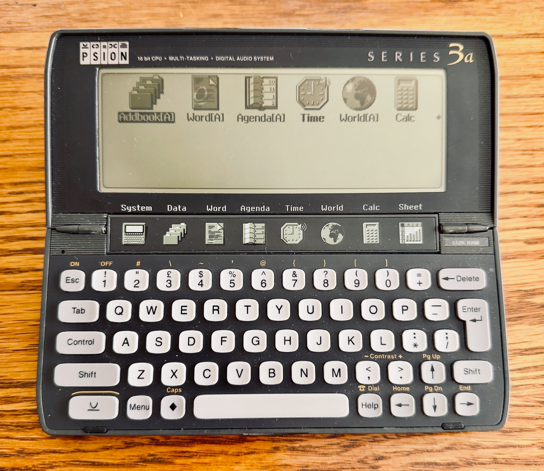 Auto-generated description: A Psion Series 3a handheld device is open on a wooden surface, displaying icons on its screen.