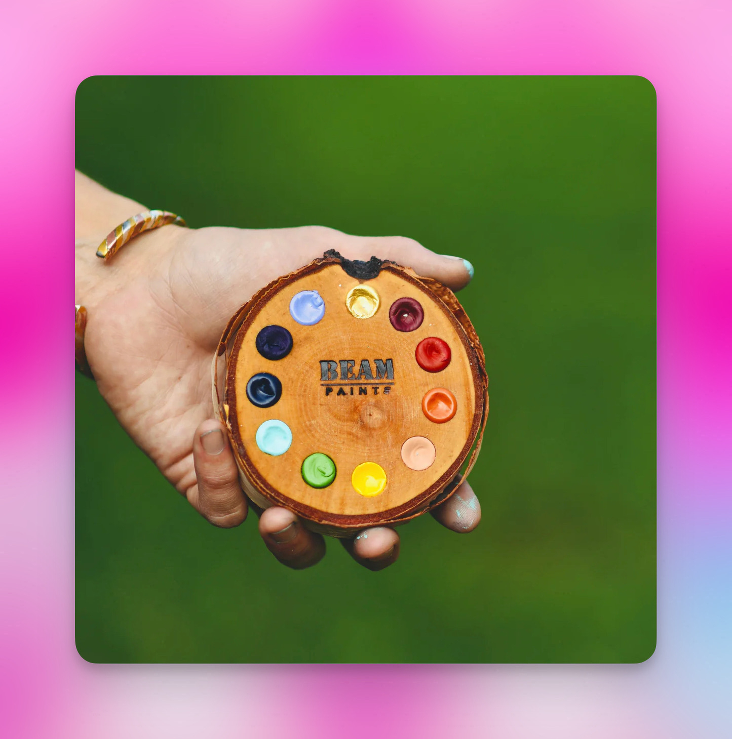 Auto-generated description: A hand holds a circular wooden palette featuring colorful paints arranged around its edge.