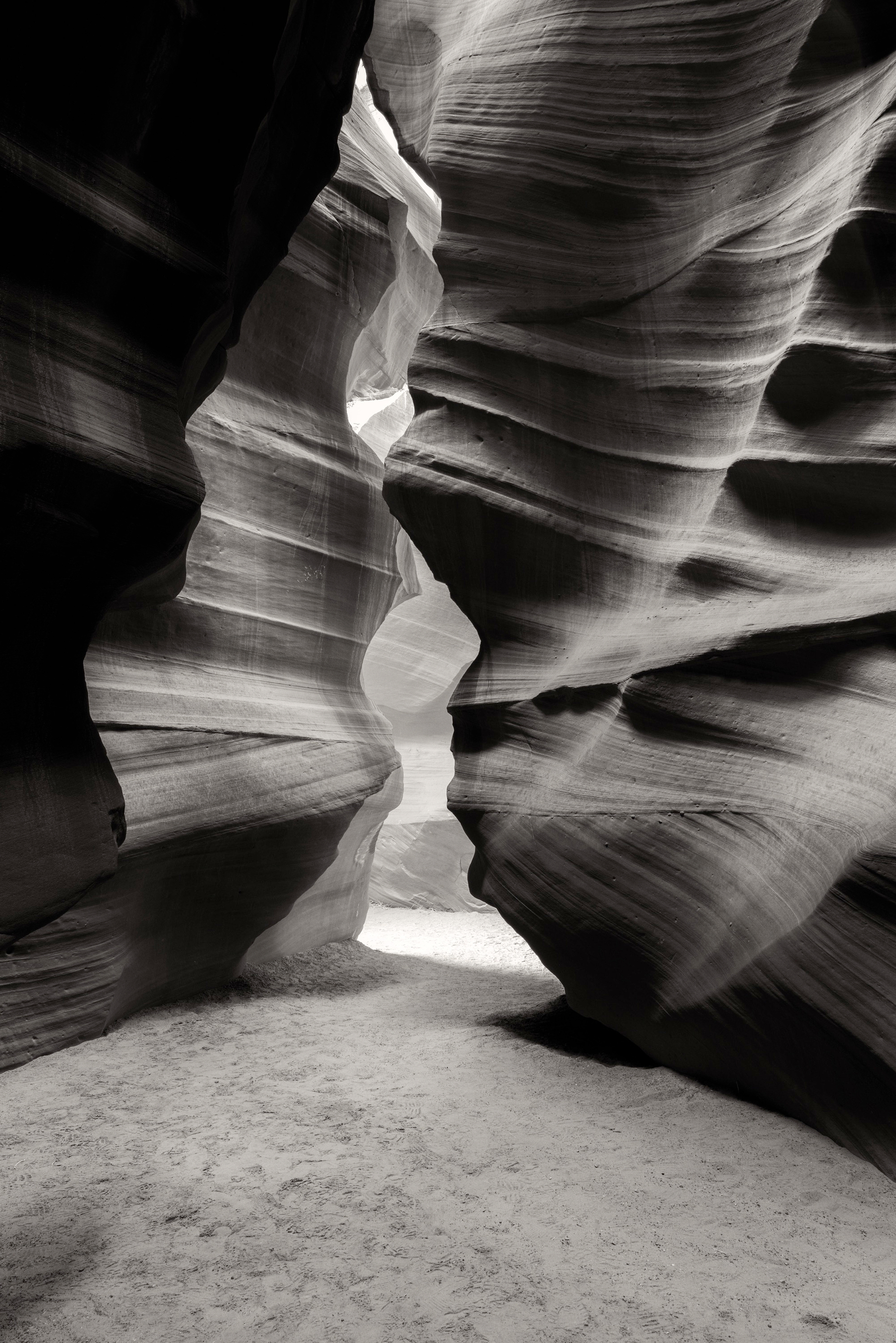 Auto-generated description: A narrow slot canyon with smooth, swirling rock formations and a view of light illuminating the passageway.