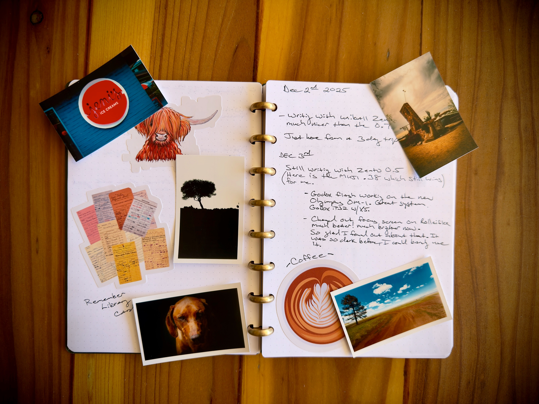 Auto-generated description: An open notebook on a wooden surface is surrounded by various photos, cards, and a collection of notes, with handwritten entries and a drawing of a coffee cup on the pages.