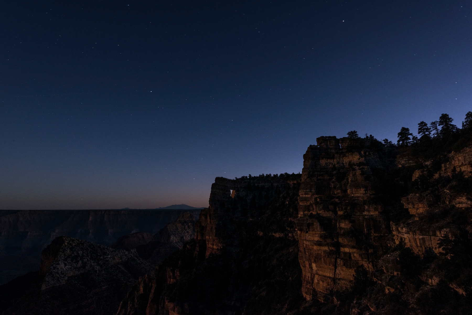 Auto-generated description: A rocky canyon is silhouetted against a starry night sky with a subtle gradient of twilight.