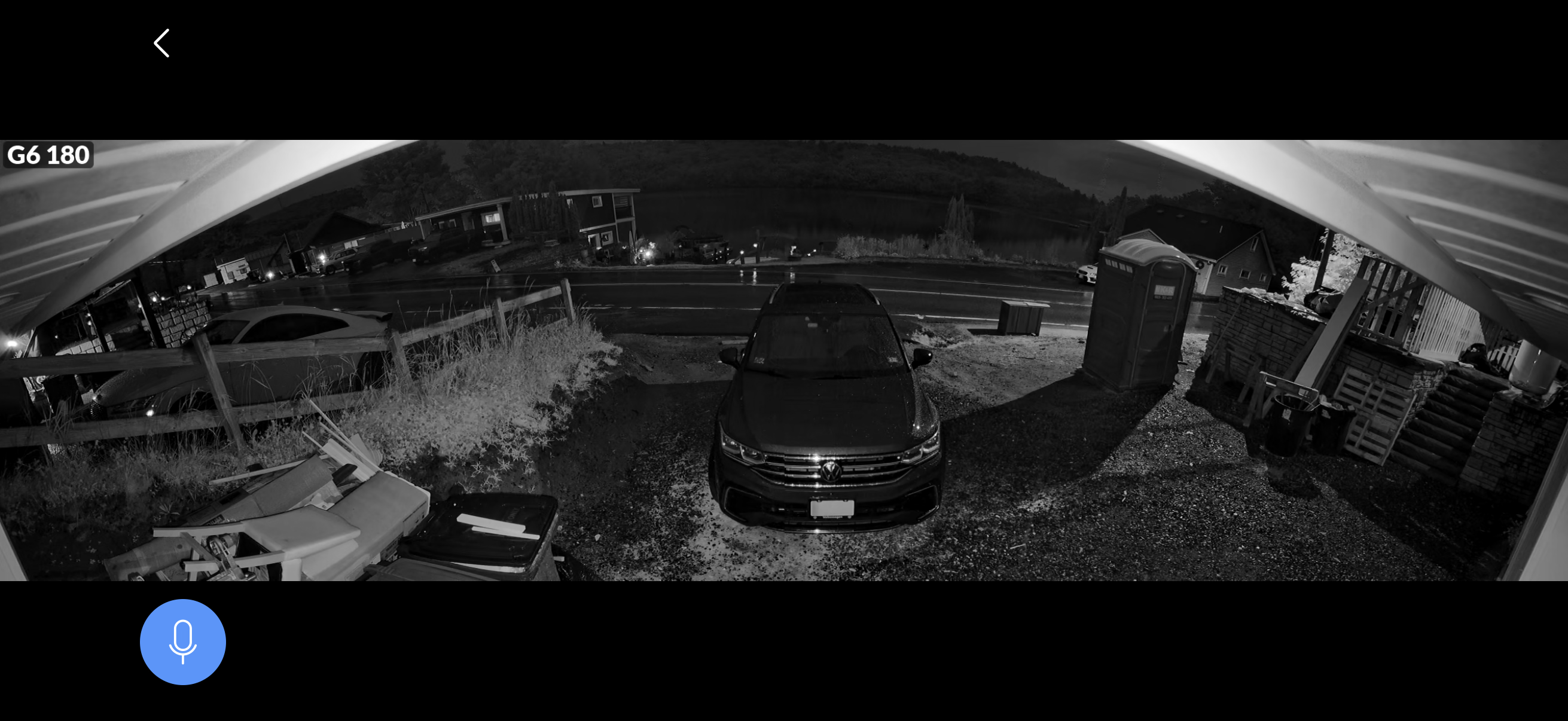A black and white night-time view from a porch shows a parked car, a portable toilet, and various outdoor items scattered around.