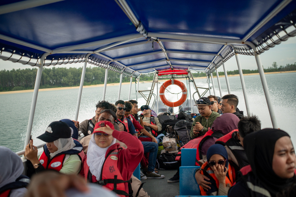 A group of people wearing life jackets are sitting on a tour boat navigating through calm water.