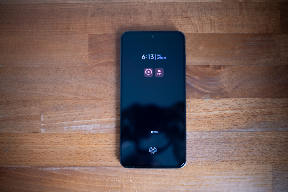 A smartphone displaying a lock screen with the time, icons, and a fingerprint symbol is placed on a wooden surface.