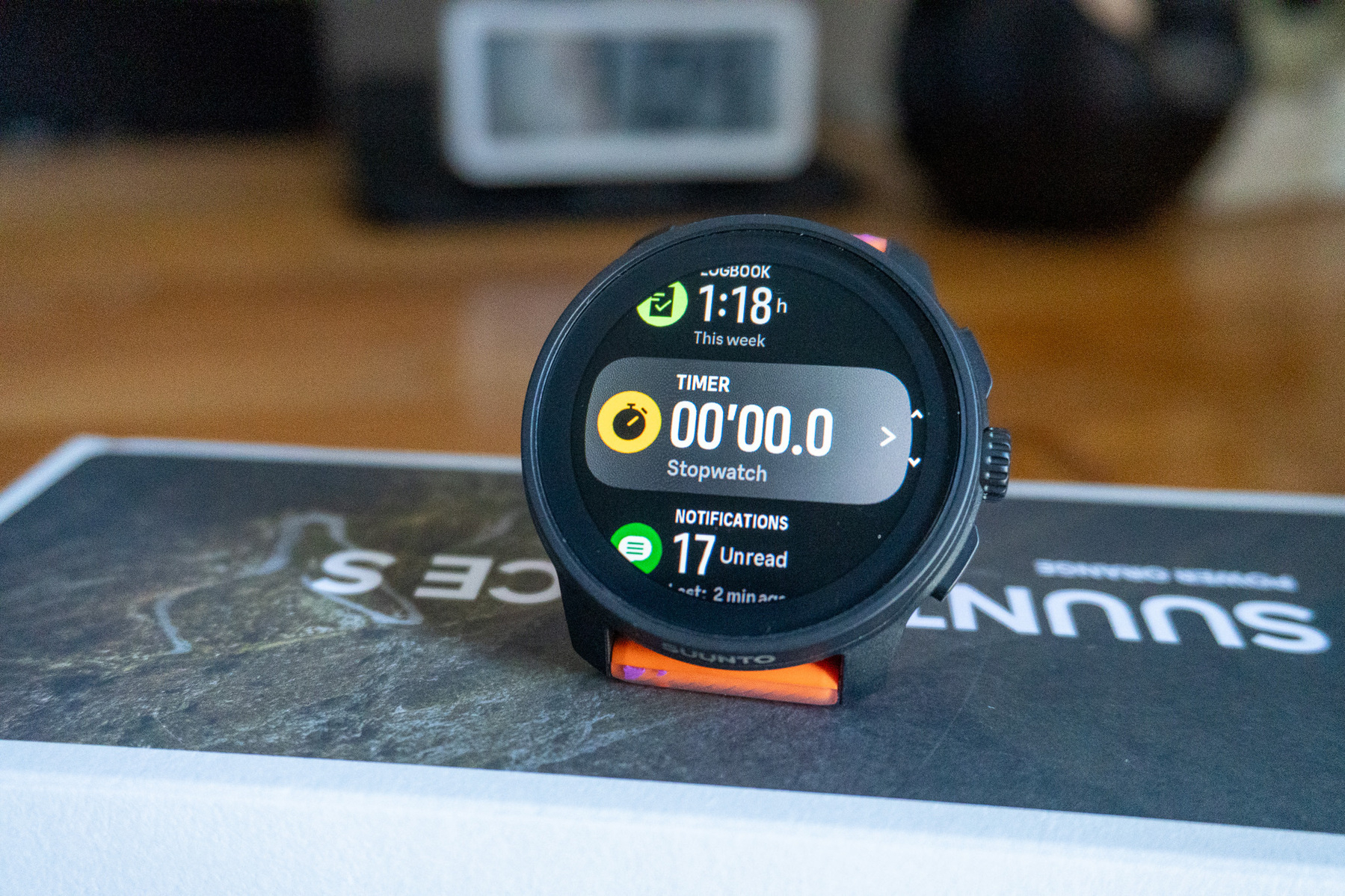 A smartwatch displaying various features like the timer, notifications, and a summary of the current week is resting on a box.