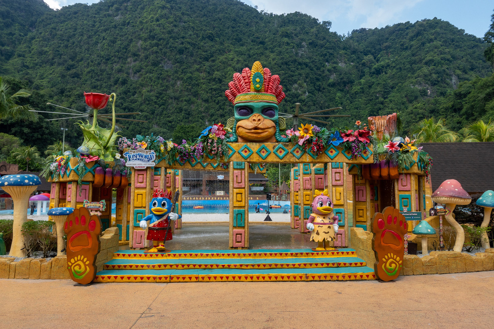 A colorful, themed entrance with cartoon characters leads to a water park set against a backdrop of lush green hills.