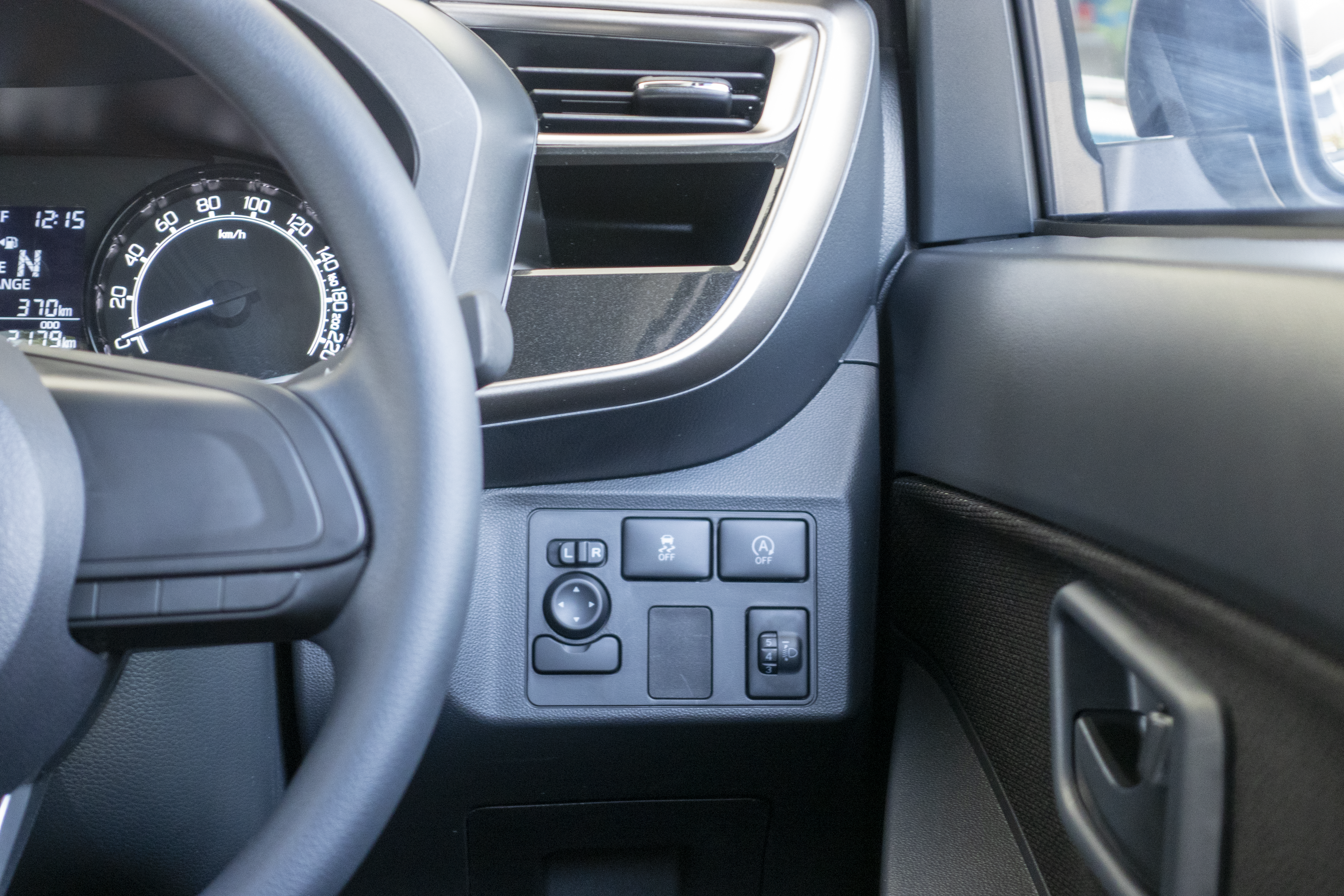 A car's interior focuses on the steering wheel, dashboard controls, and part of the door.