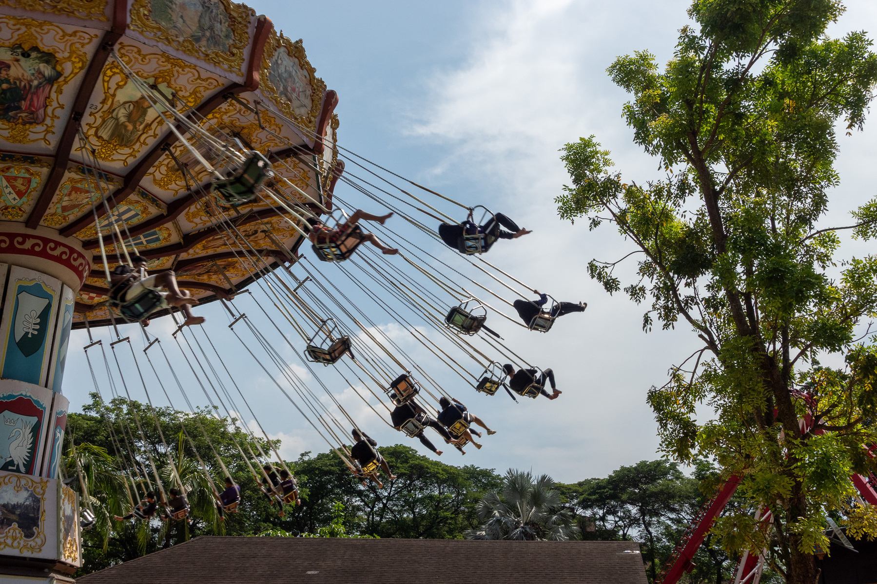 People are enjoying a swing ride at an amusement park with a backdrop of trees and a partly cloudy sky.