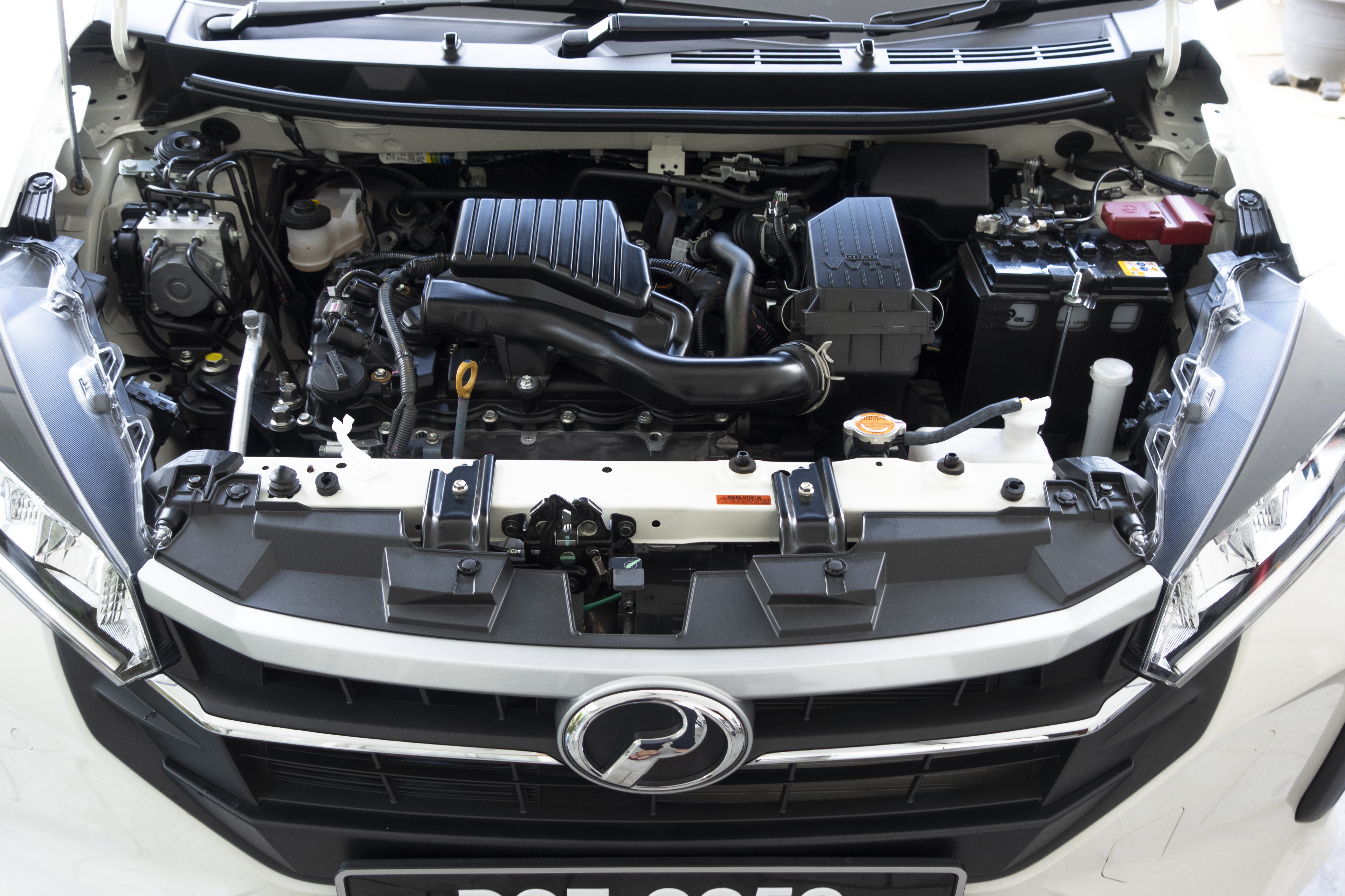 A car engine is displayed with various components visible under the hood, including belts, a battery, and air filter housing.