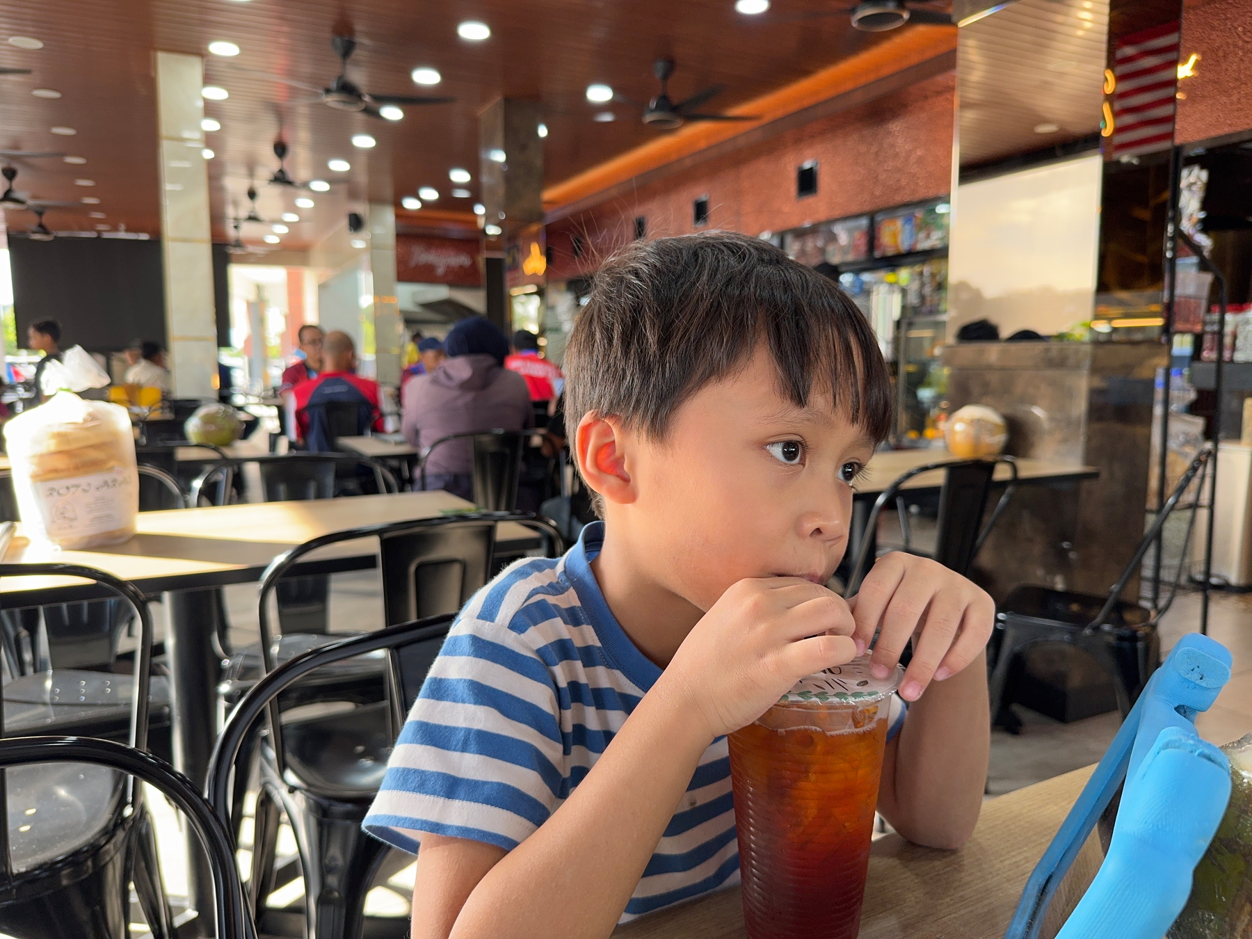 A child is sitting at a table in a restaurant, drinking from a cup with a straw.