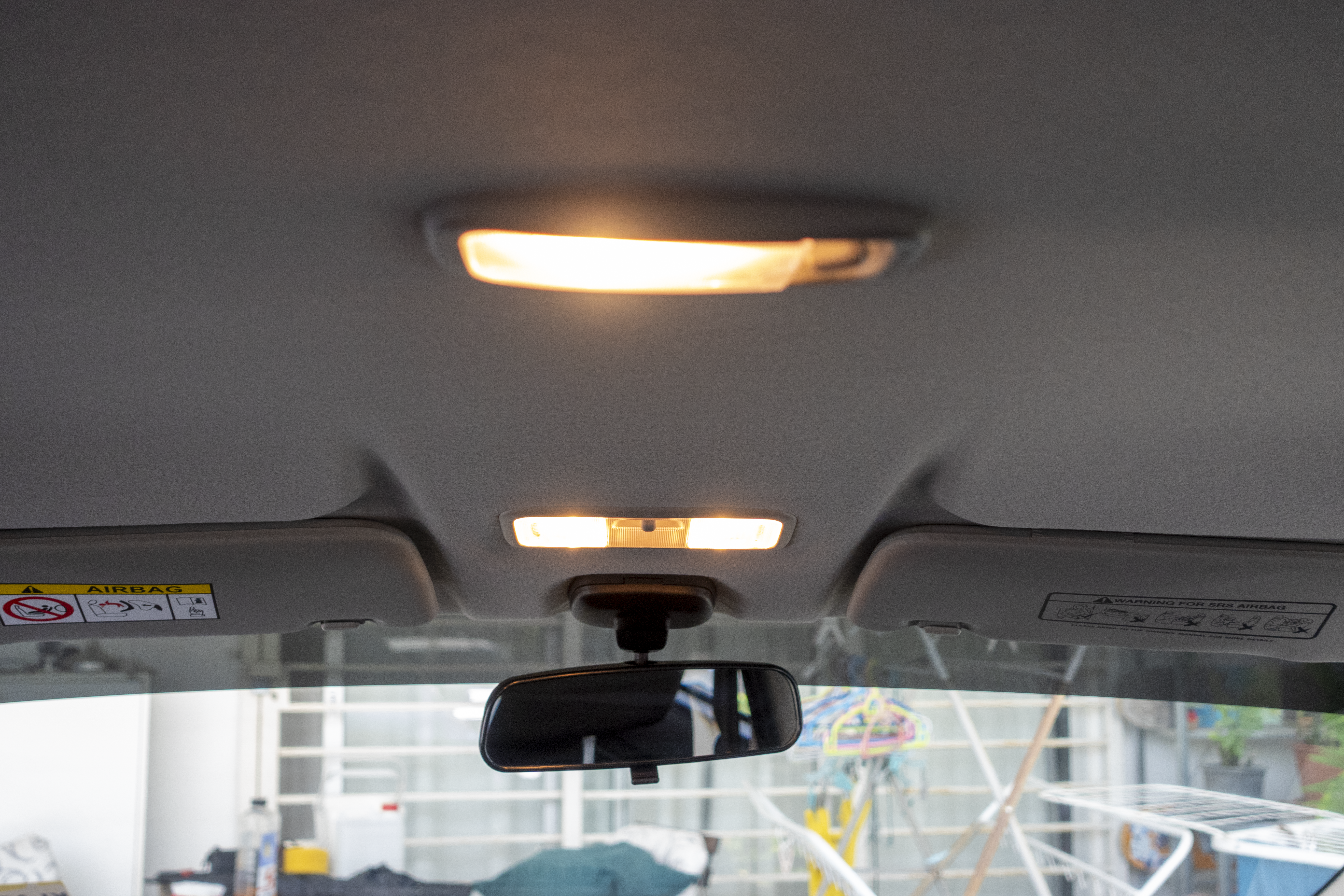 Car interior roof with two dome lights turned on and a rearview mirror visible.
