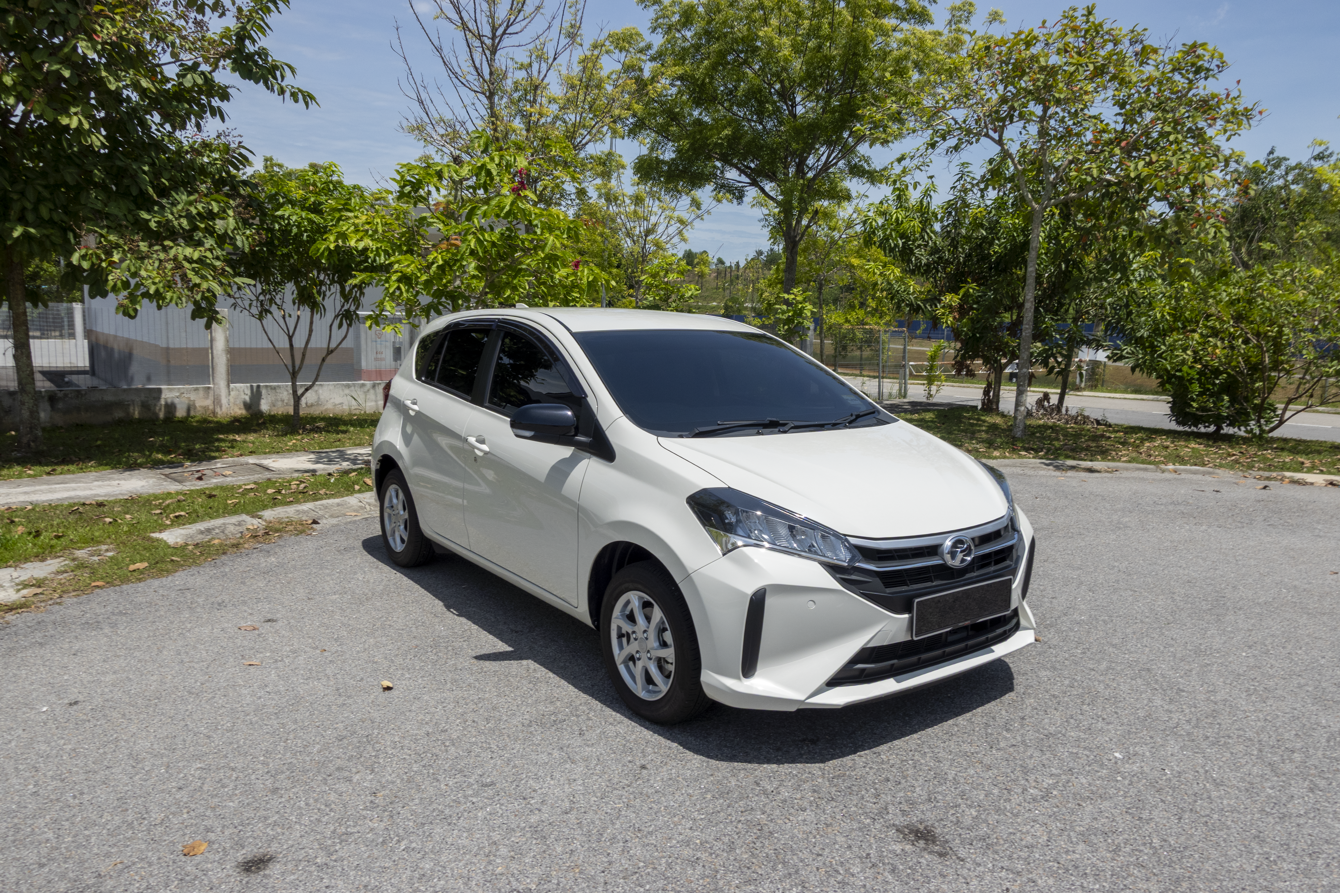 A white car is parked on a paved area surrounded by trees and greenery.