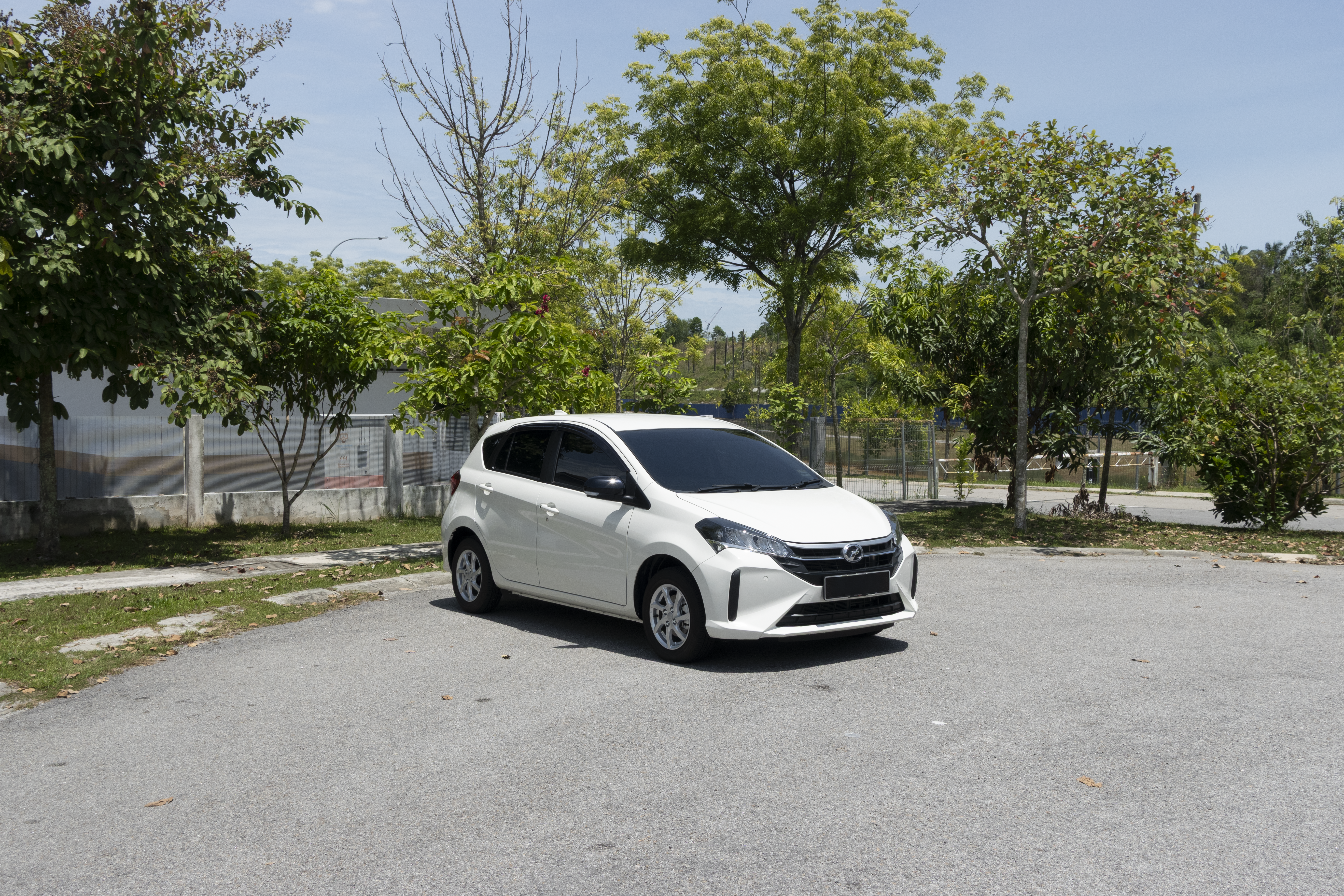 A white car is parked on a paved area surrounded by trees and greenery.