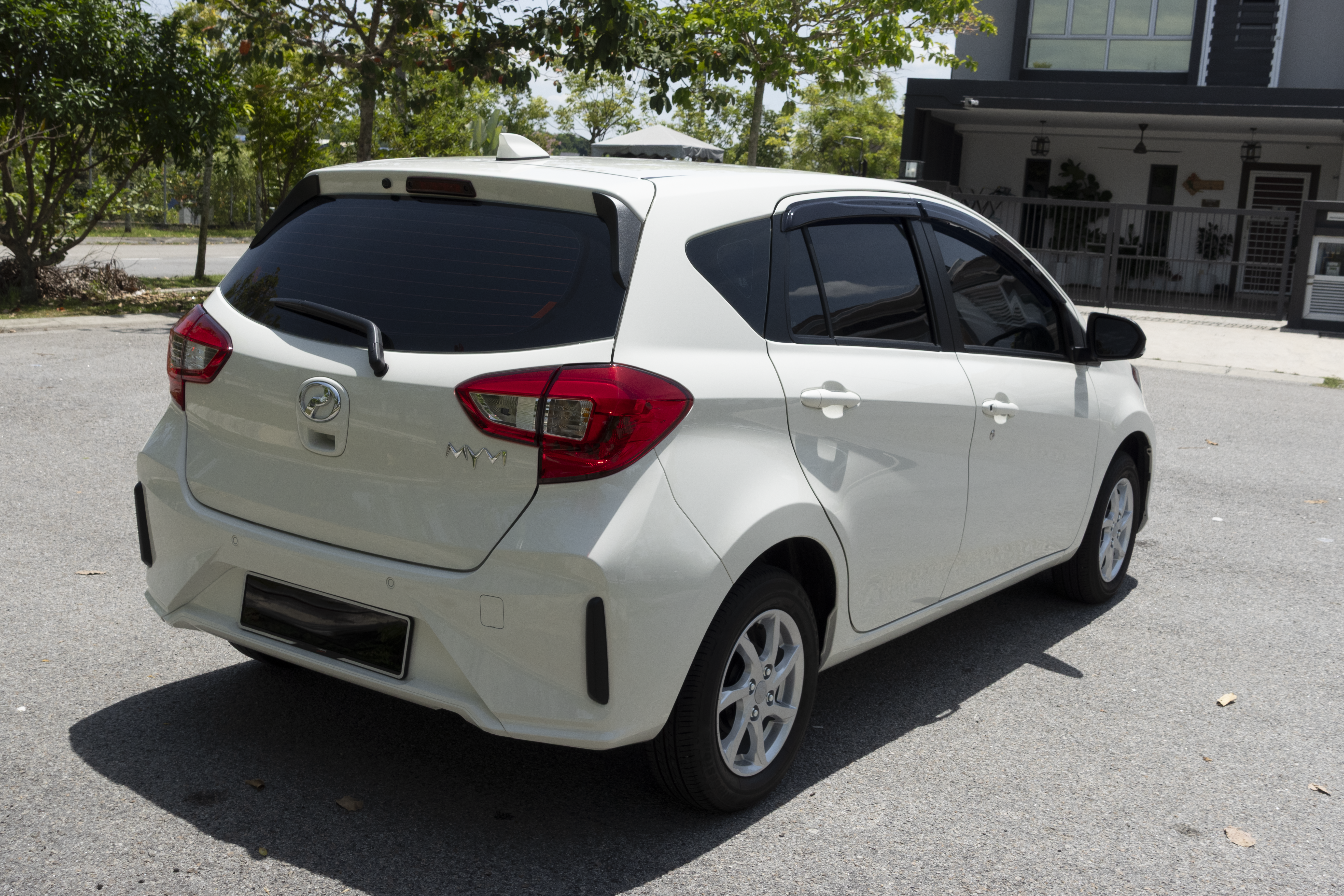 A white compact car is parked on a street near trees and a building.