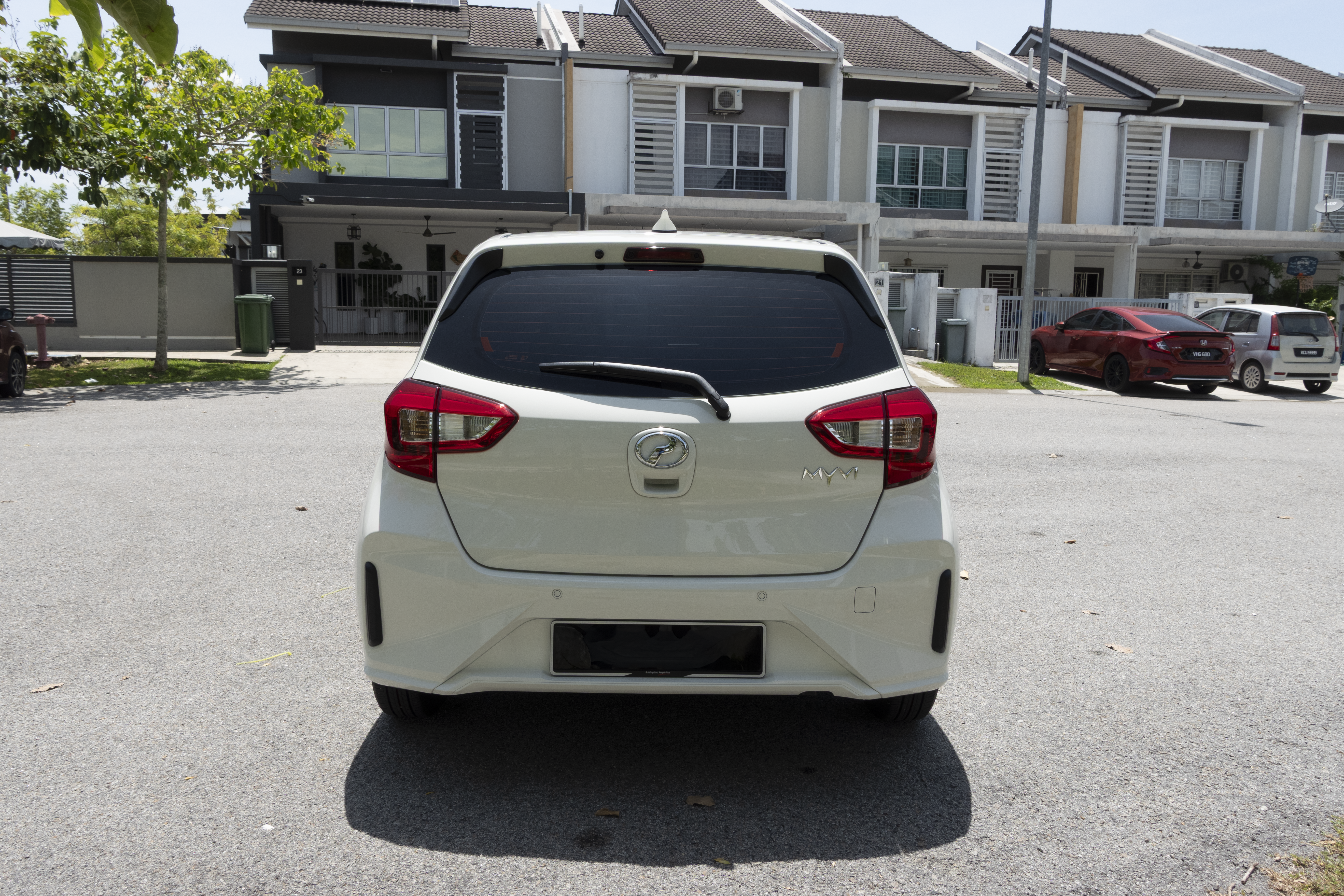A white car is parked in a residential neighborhood with modern two-story houses in the background.