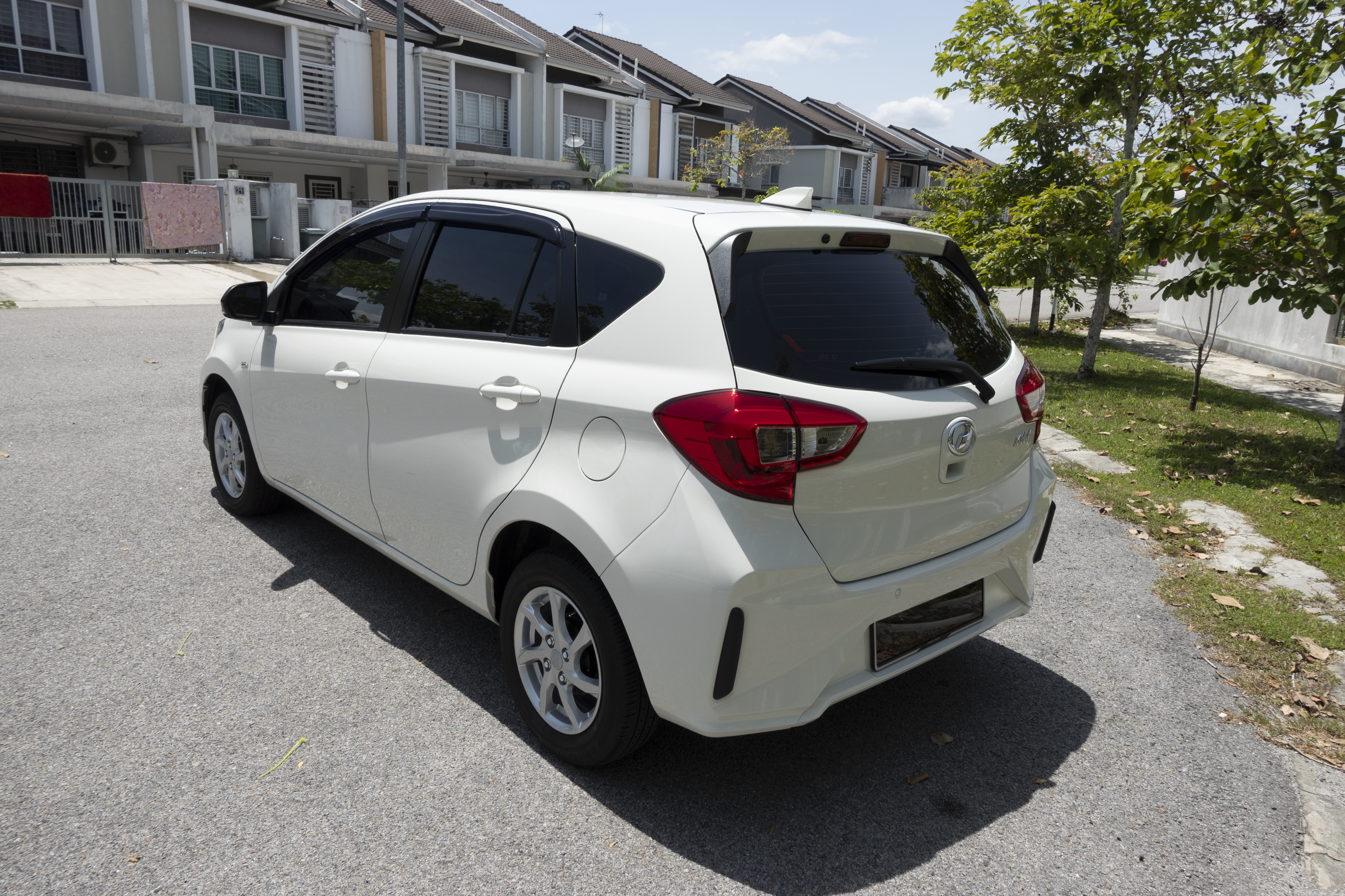 A white hatchback car is parked on a residential street near row houses under a clear sky.