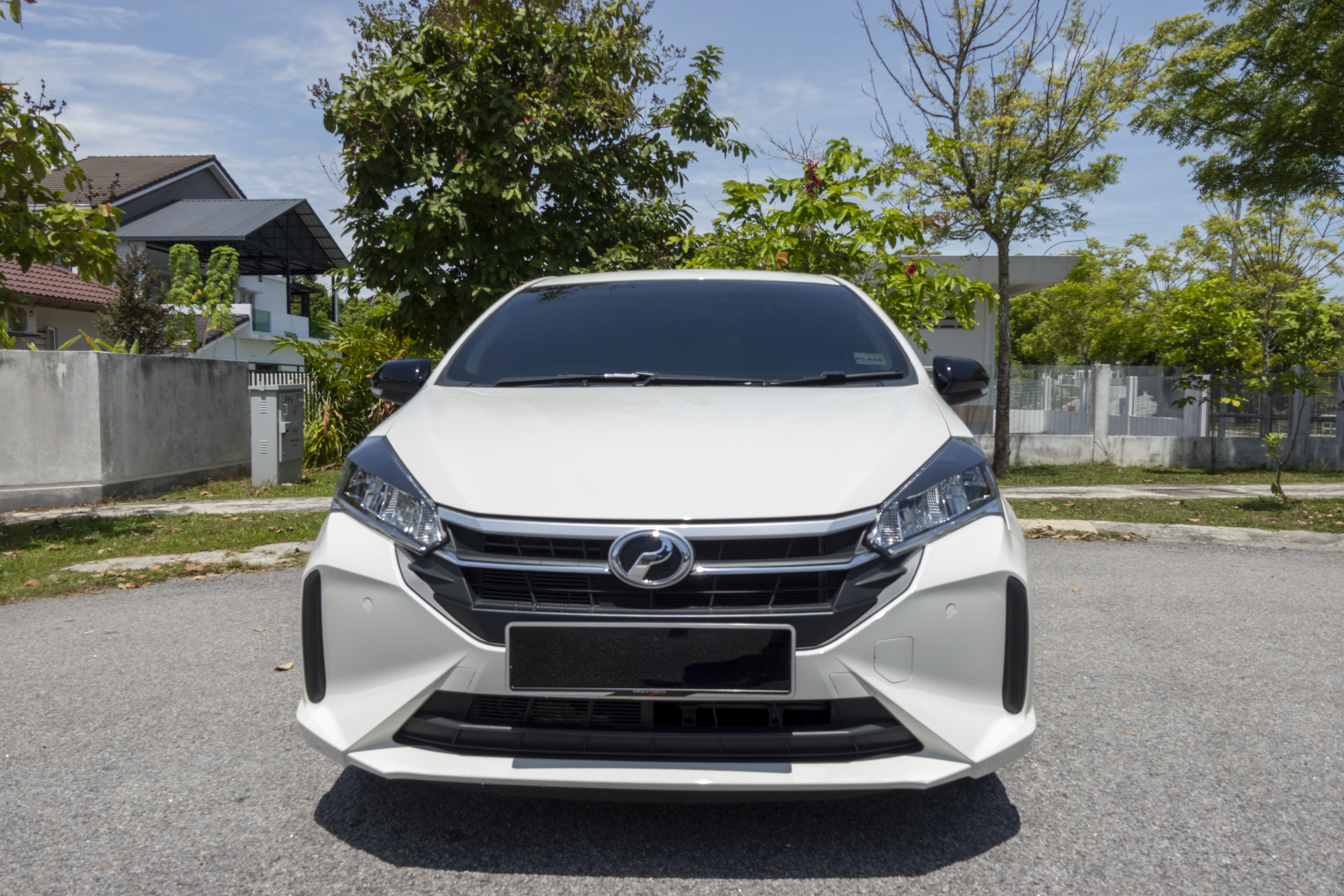 A white car is parked on a residential street surrounded by trees and houses.