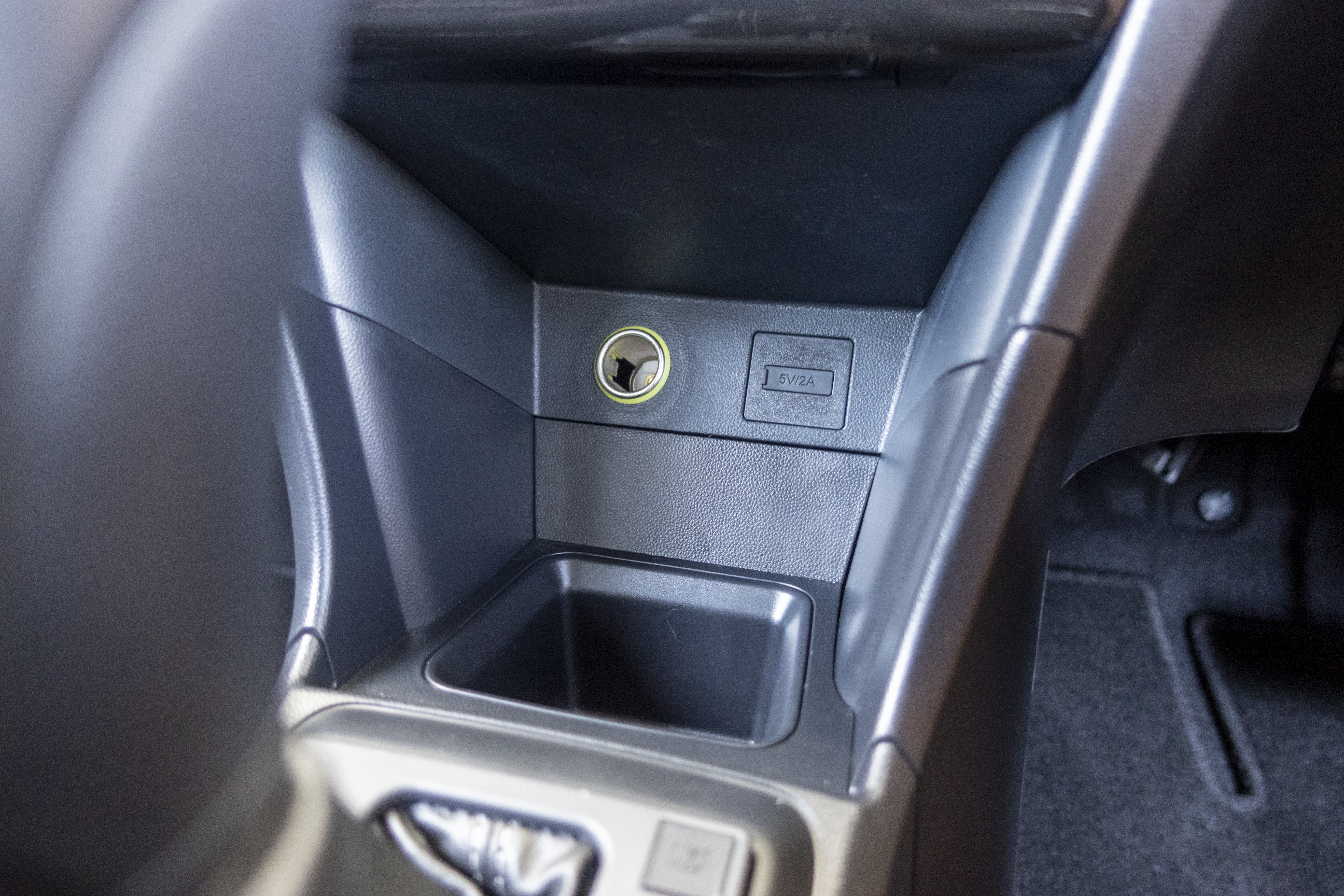 A car's interior console featuring a cigarette lighter socket and a small storage compartment is visible.