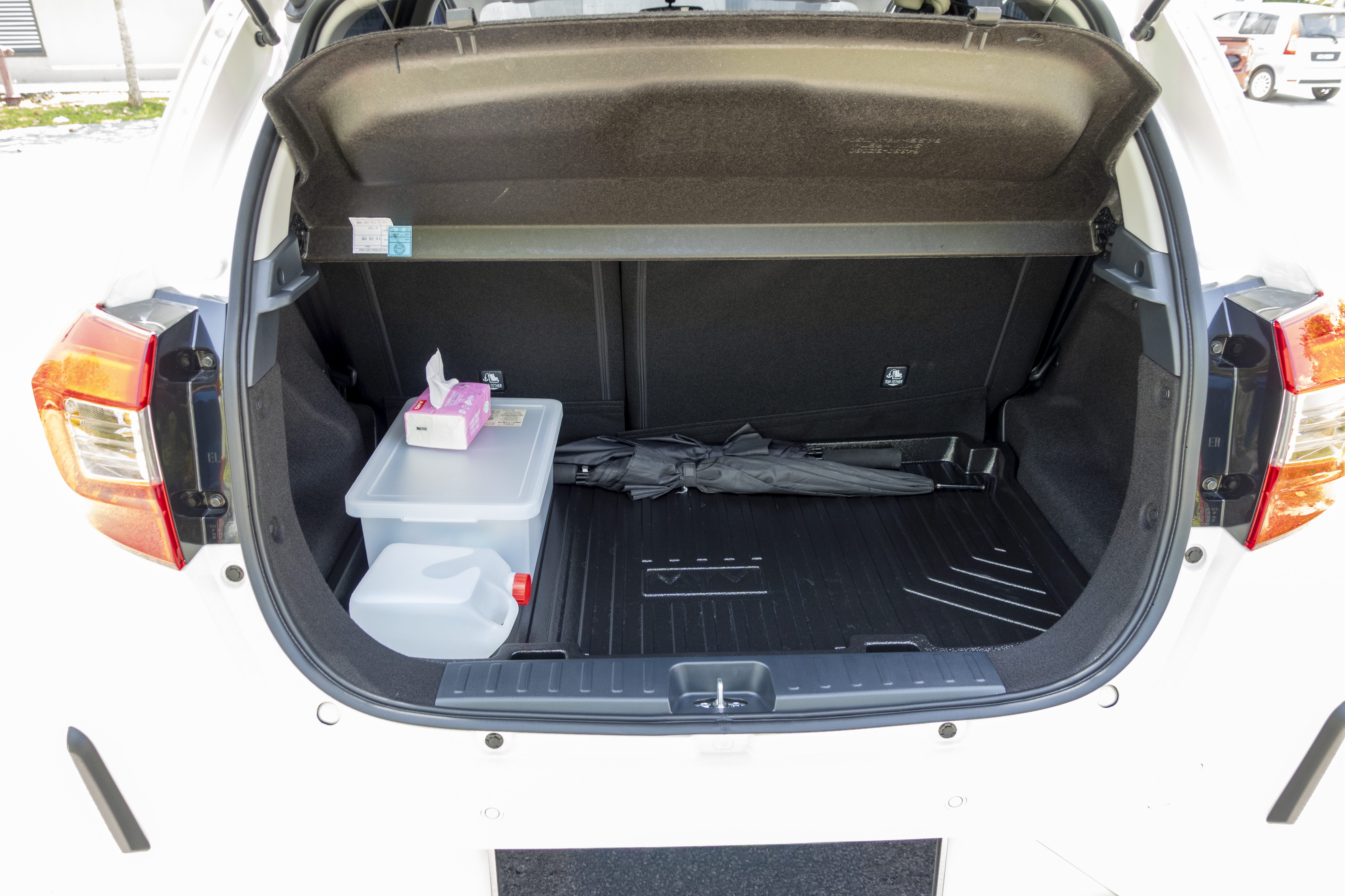 A car trunk contains a storage box with a tissue box on top, a large bottle, and an umbrella placed inside.