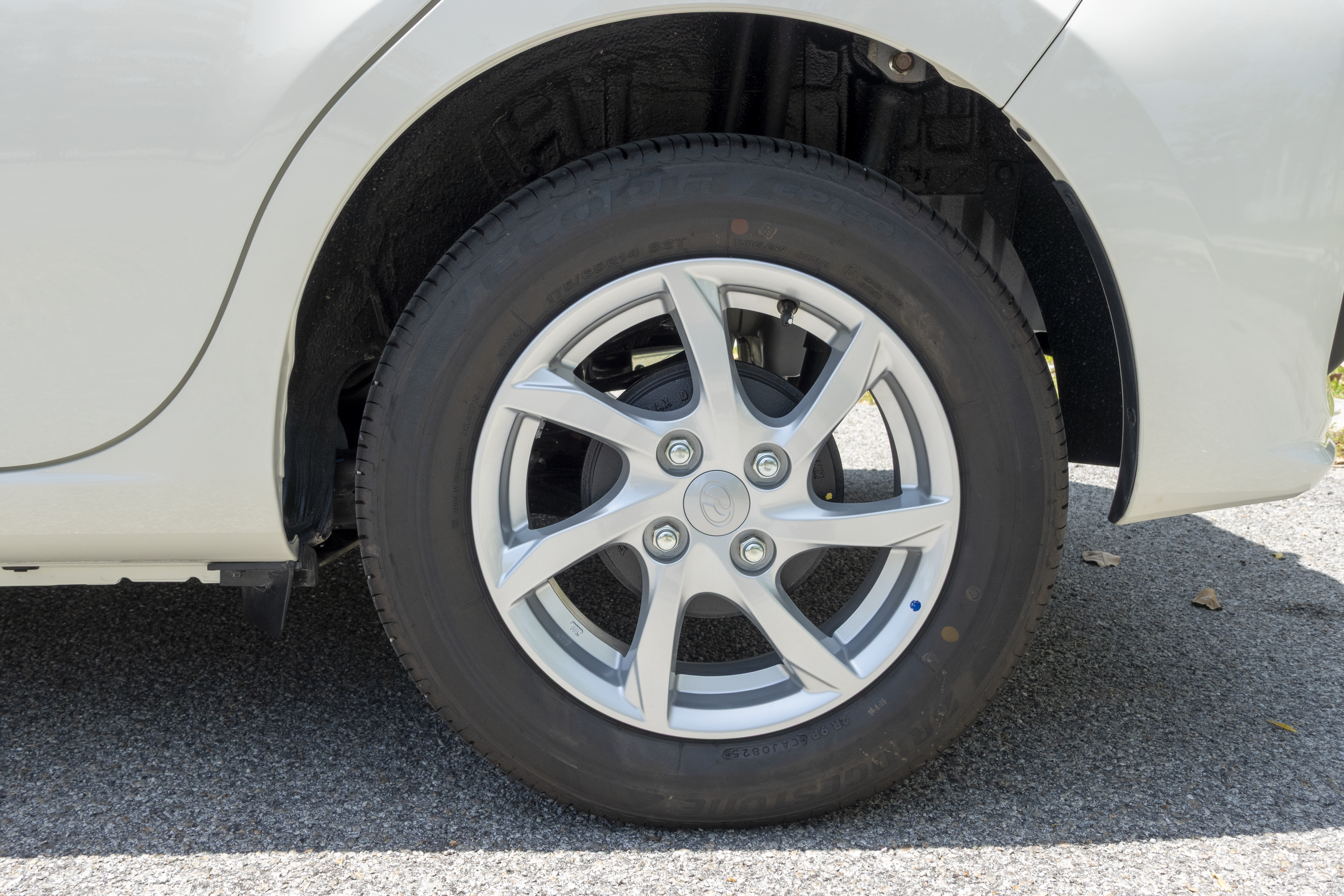 A car's rear wheel with a silver alloy rim is shown on a paved surface.