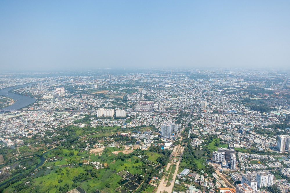 A sprawling urban cityscape with dense buildings, patches of greenery, and a river winding through the area under a clear sky.
