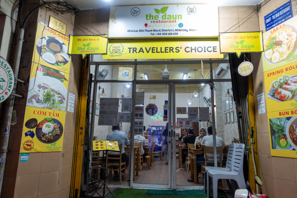 A brightly lit Vietnamese restaurant named The Đaun welcomes diners with colorful food posters and a Travellers' Choice sign above the entrance.
