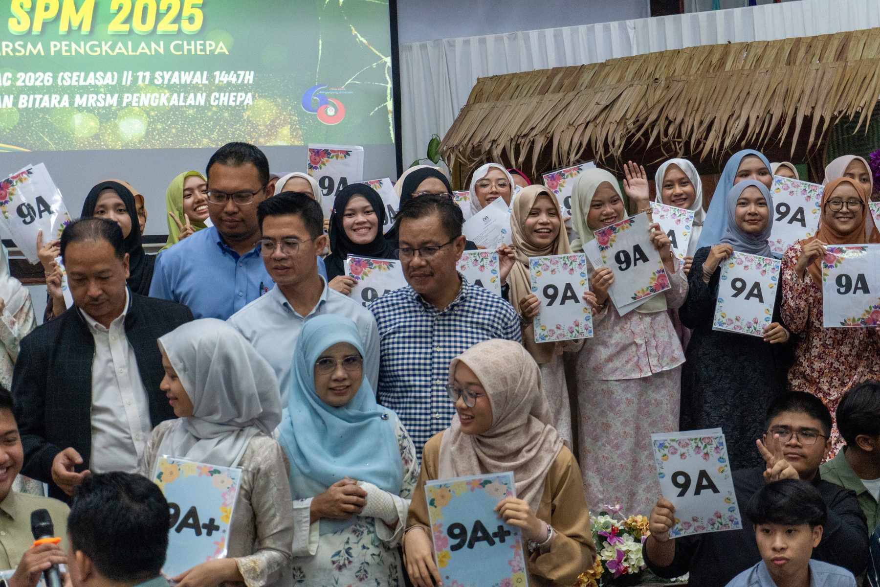 A group of people are holding certificates and signs with 9A+ on them at a gathering or celebration.