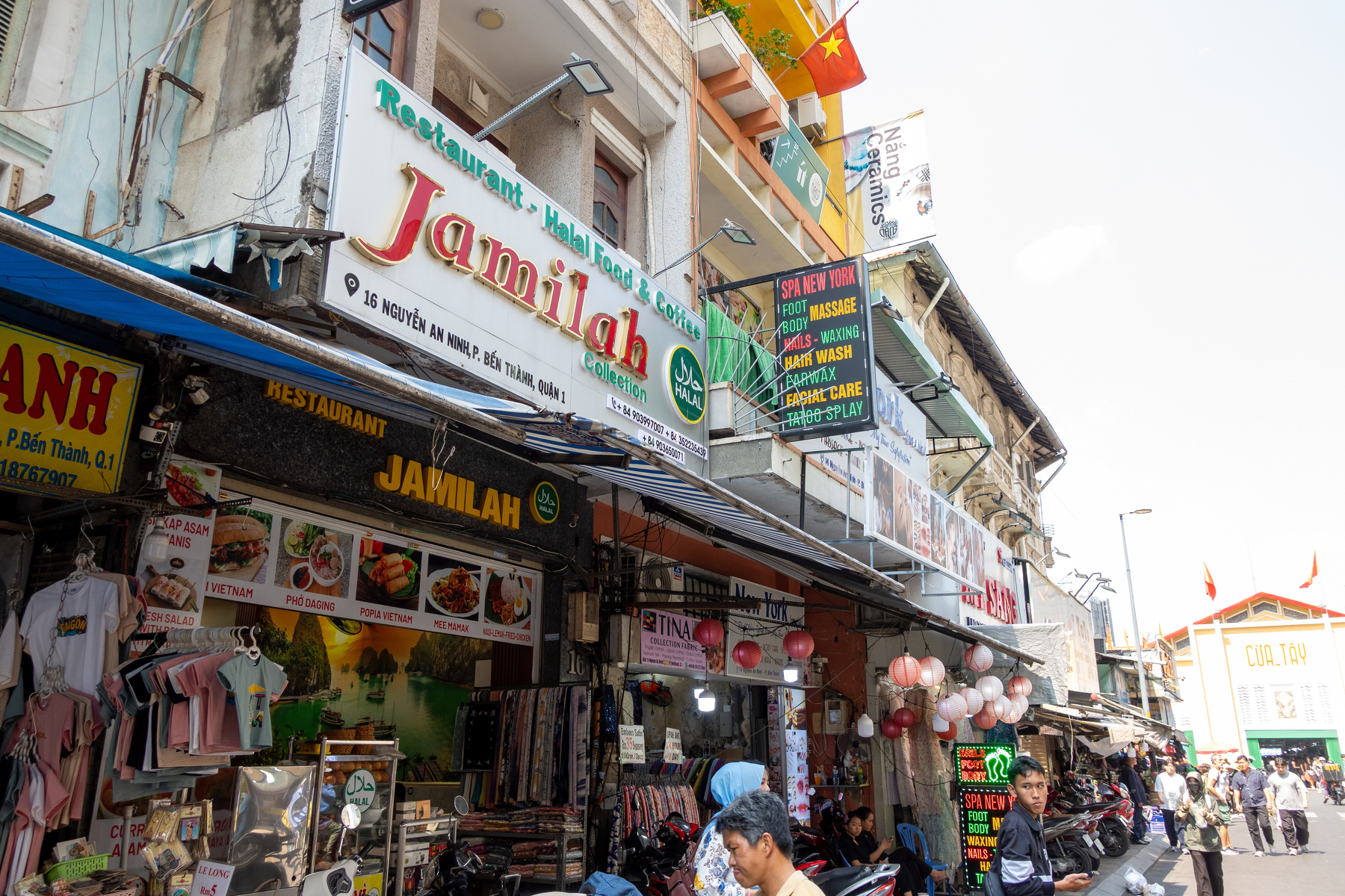 A busy street scene featuring various shops and restaurants with colorful signs and people walking along the sidewalk.