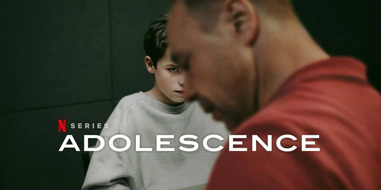 A young boy in a gray sweatshirt sits pensively at a table, with a man in a red shirt in the foreground, alongside the title ADOLESCENCE for a Netflix series.
