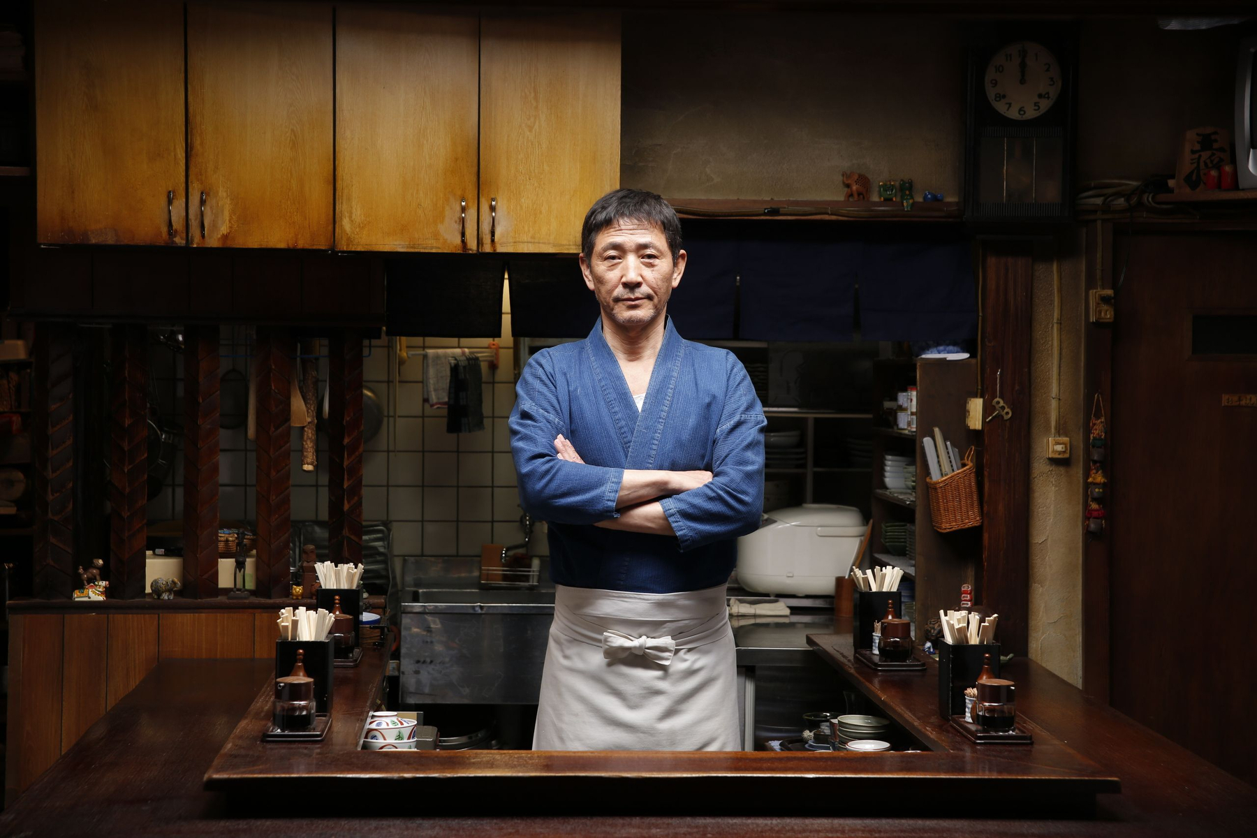 A chef stands confidently behind the counter in a cozy, traditional kitchen setting.