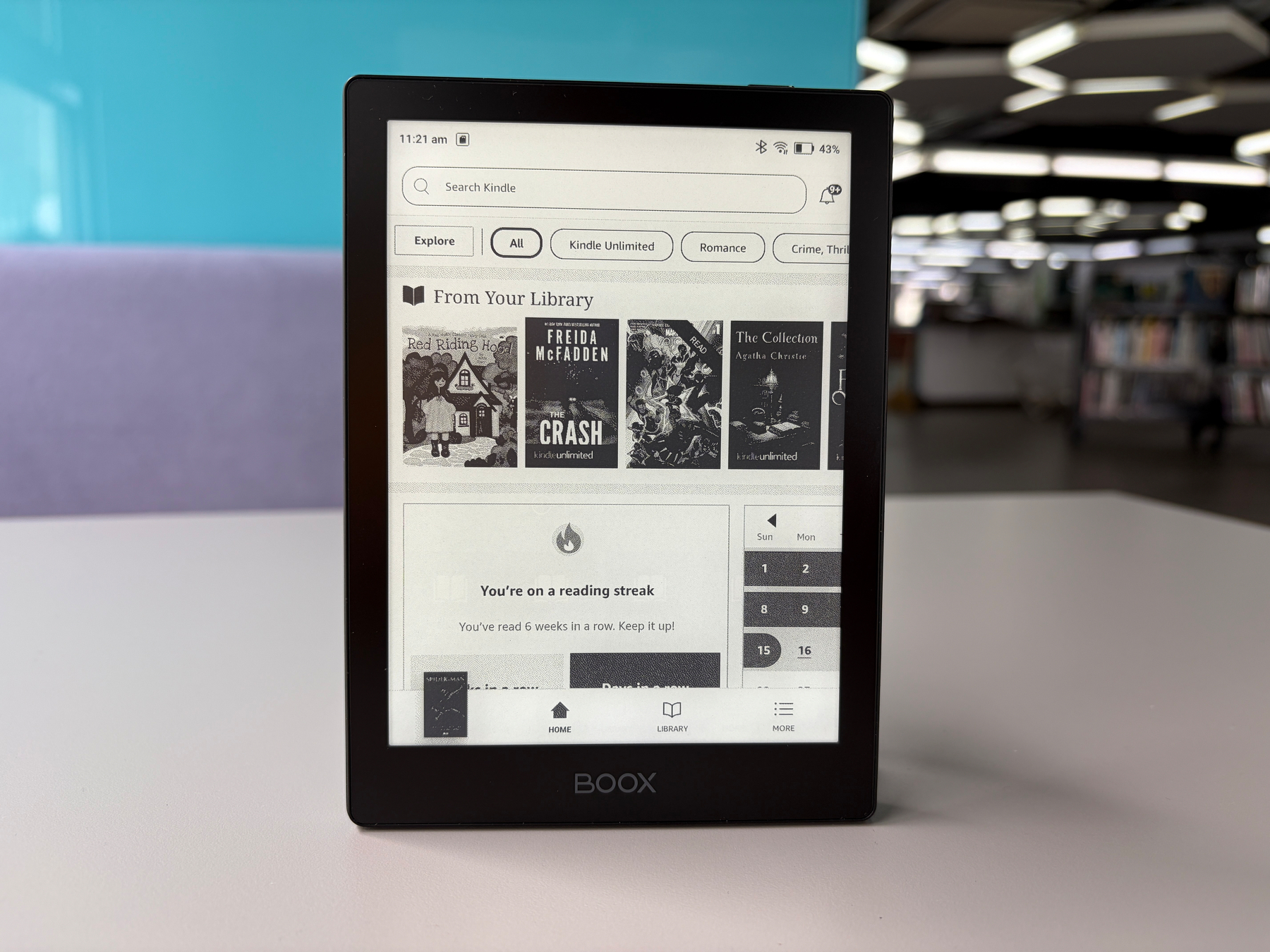 Auto-generated description: A BOOX e-reader displays a digital library interface with book covers and a notification about a six-week reading streak, set against the backdrop of a modern, well-lit room.
