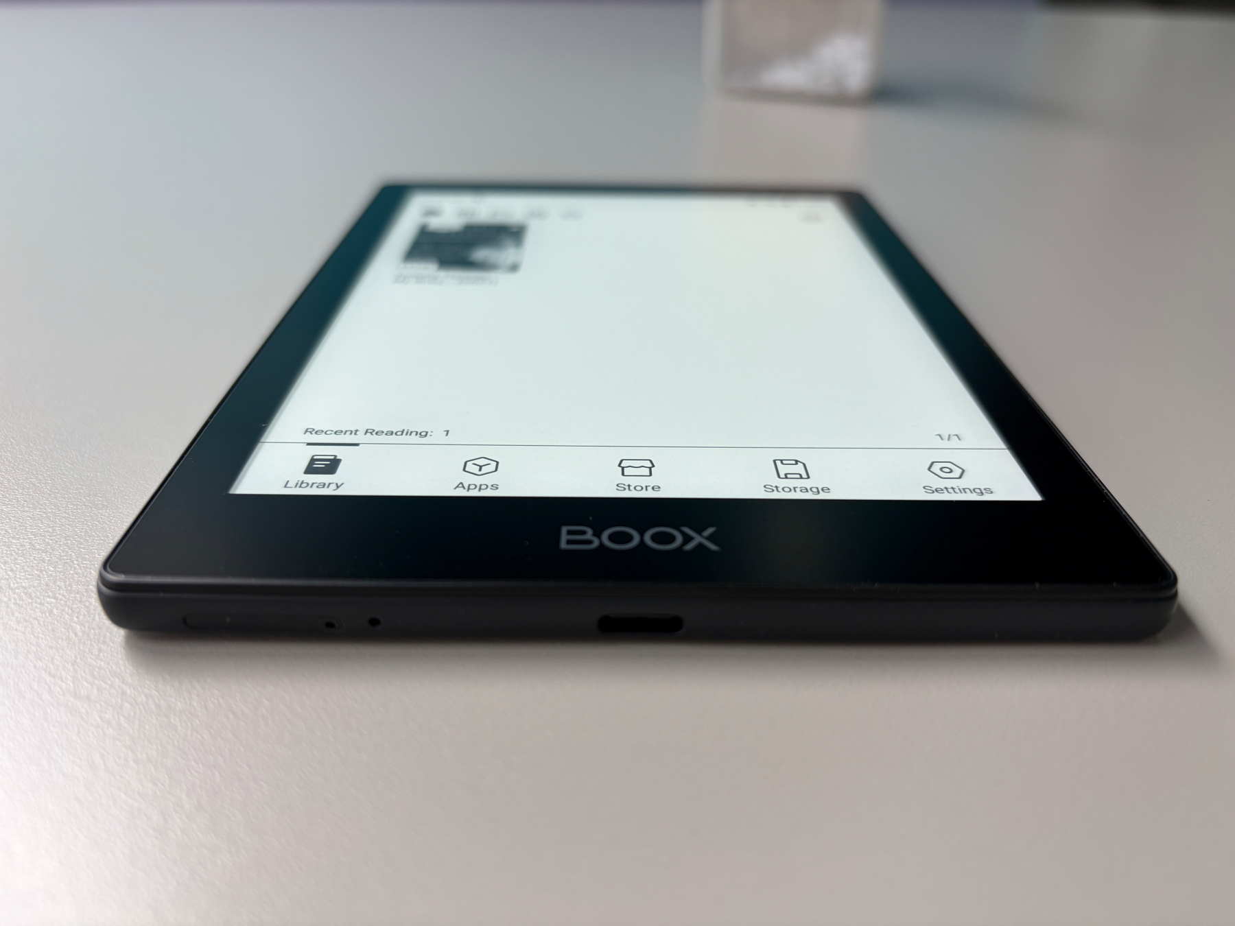 Auto-generated description: A BOOX e-reader is placed on a white surface, displaying a home screen with icons for Library, Apps, Store, Storage, and Settings.