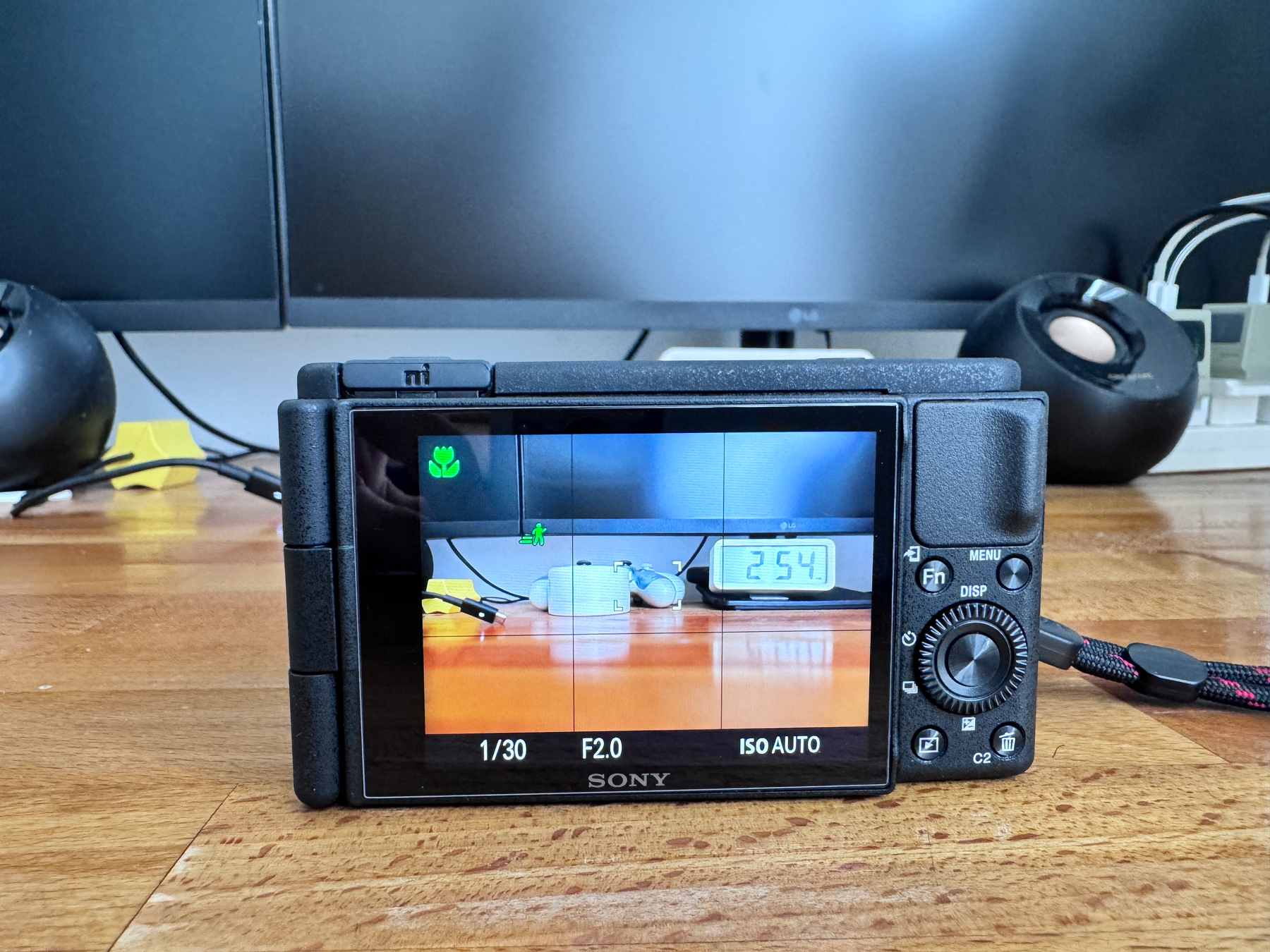 Auto-generated description: A digital camera display shows a photo of a mug, a clock, and other items on a table, with the camera settings visible at the bottom.