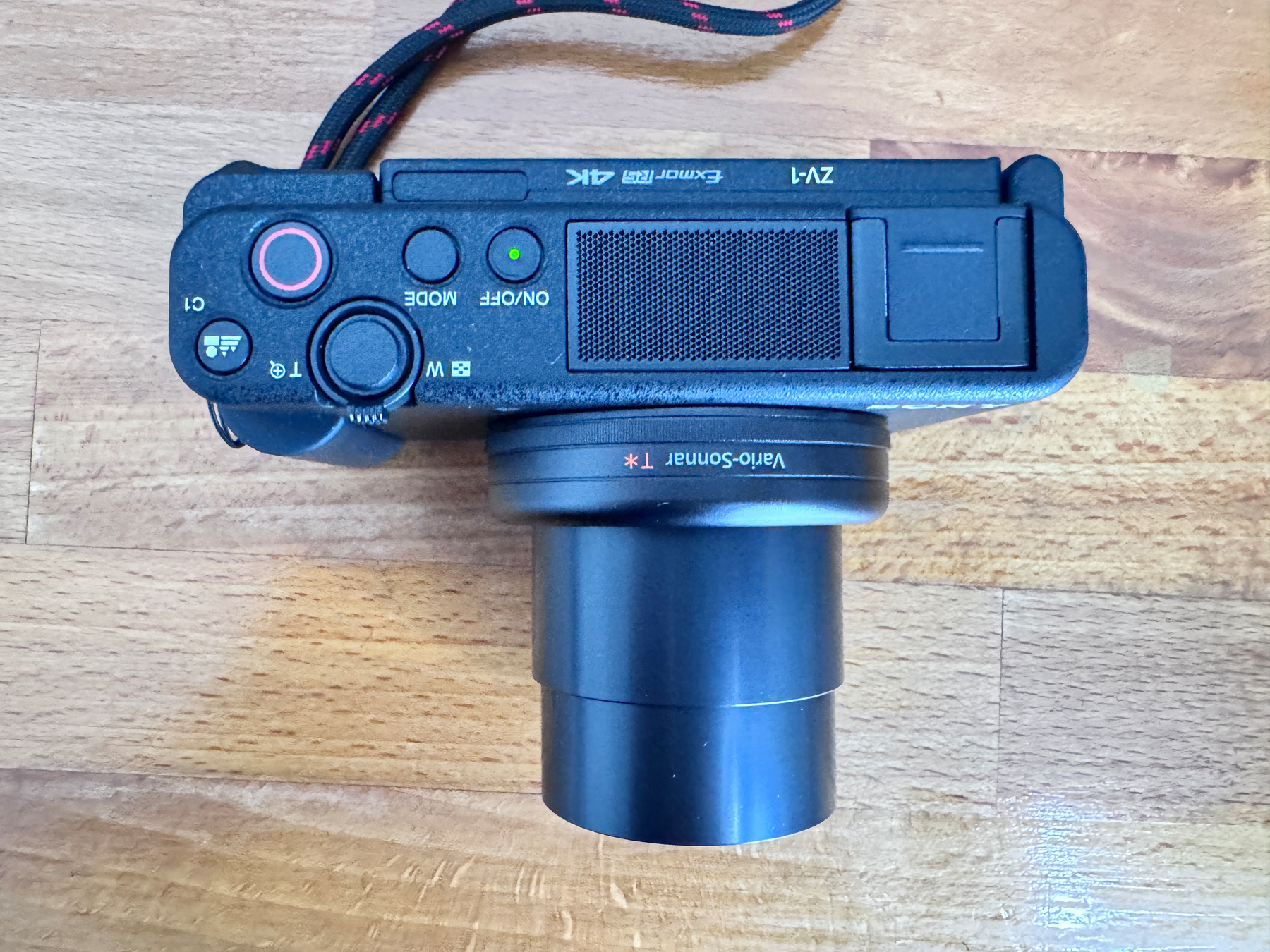 Auto-generated description: A black digital camera with an extended lens is placed on a wooden surface, viewed from the top side.