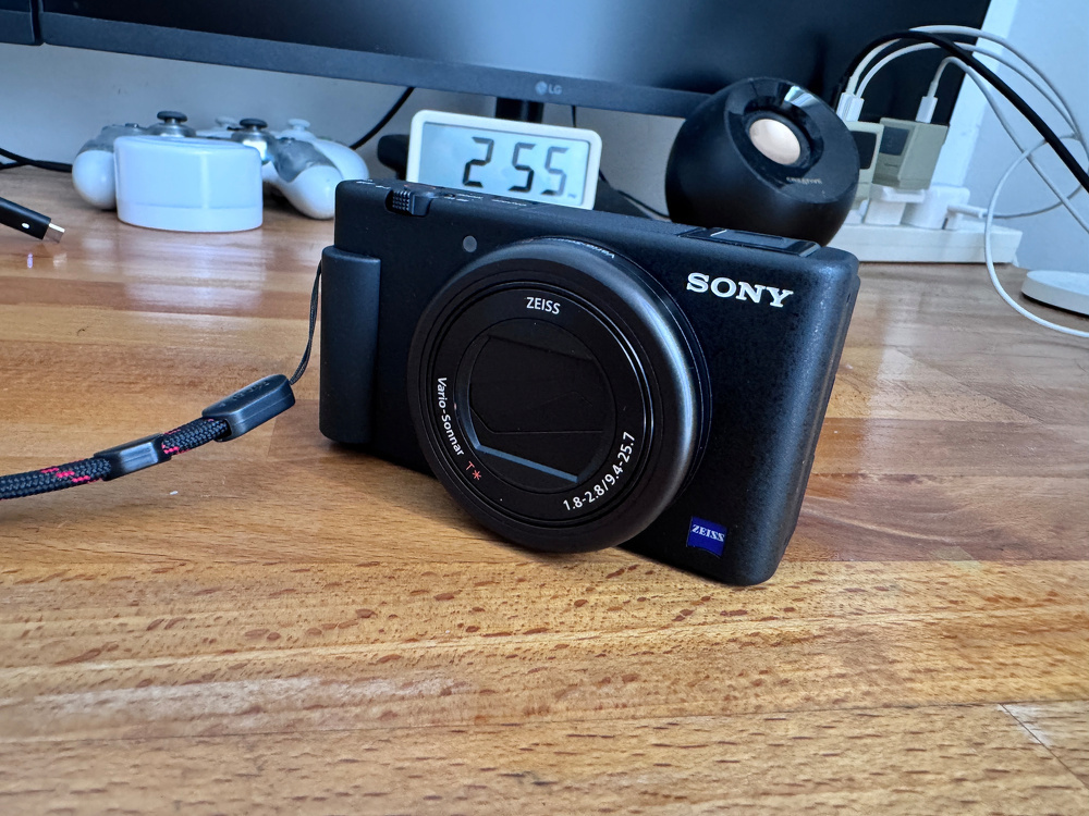 A Sony camera is placed on a wooden table, with various electronic devices in the background.