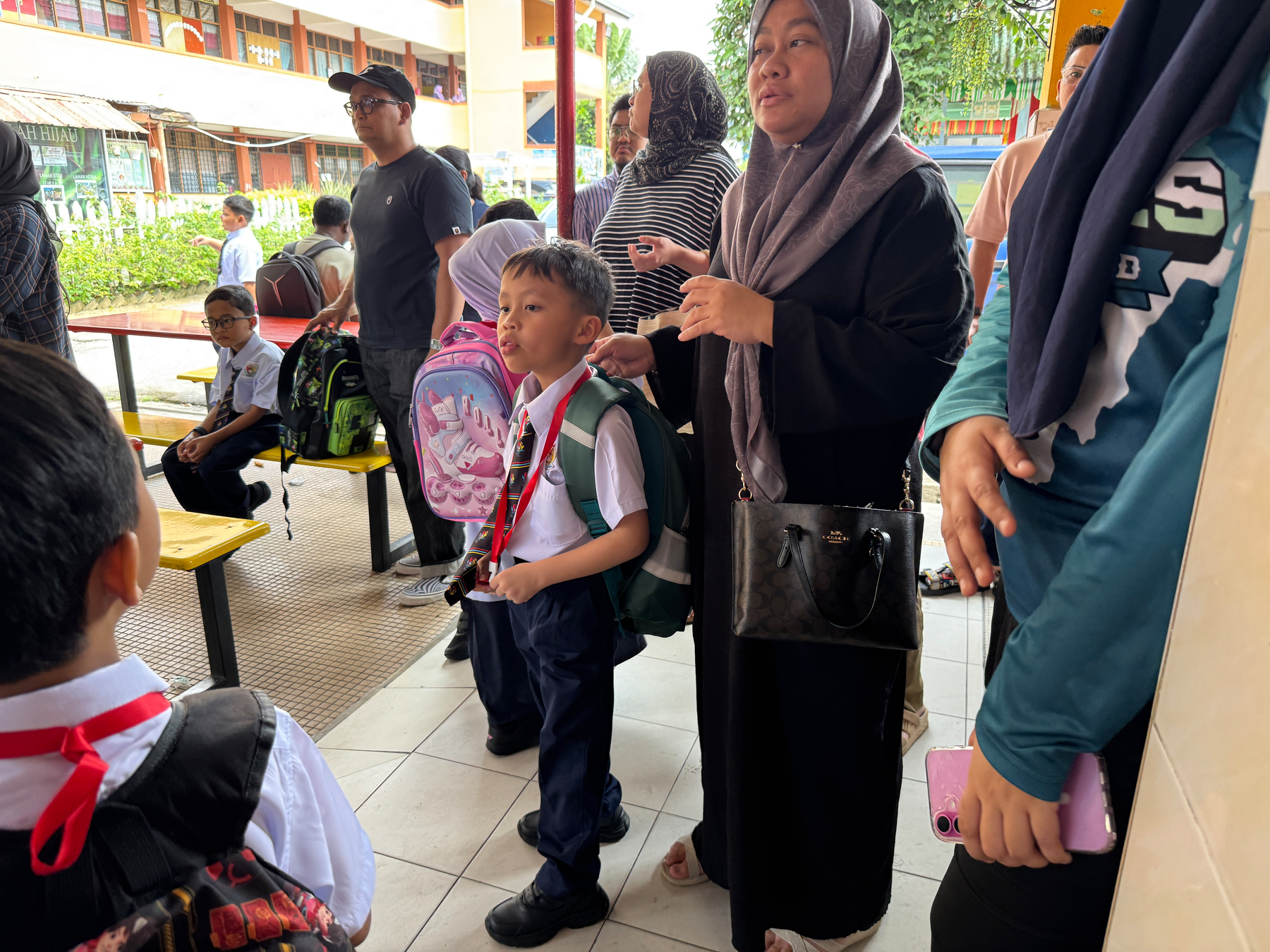 Auto-generated description: A group of people, including children in school uniforms and adults, are gathered in a school setting.