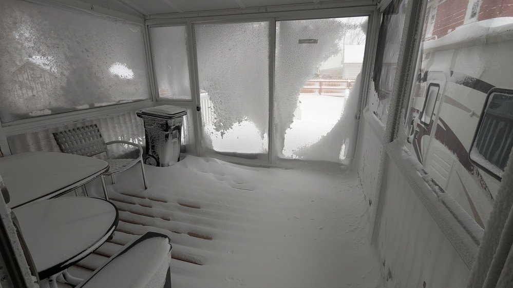 A snow-covered enclosed porch features patio furniture and a view obstructed by frosted glass.