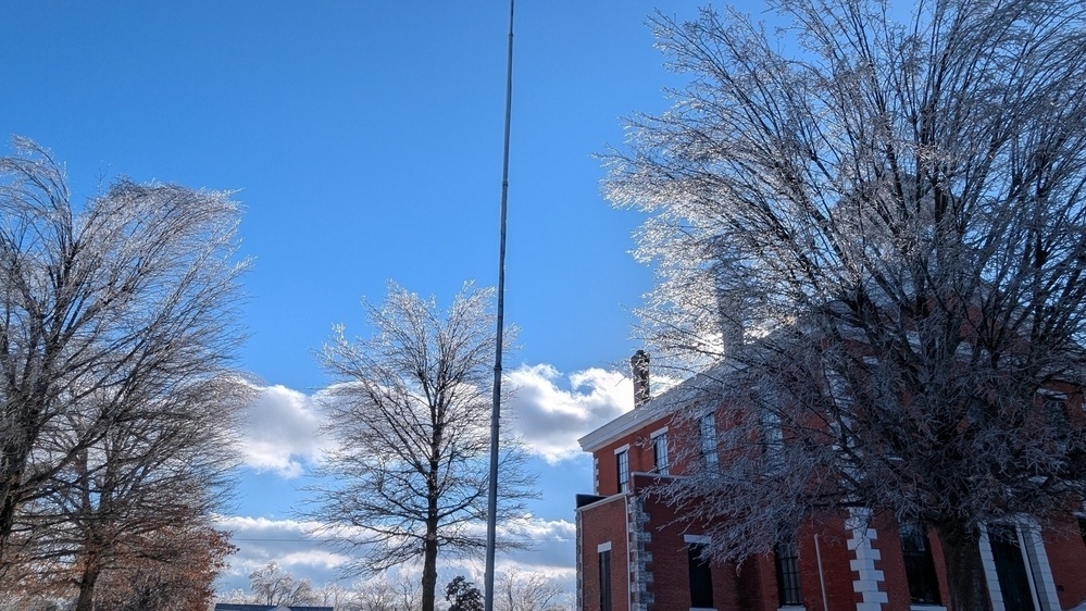 A brick building is surrounded by trees covered in ice under a clear blue sky.