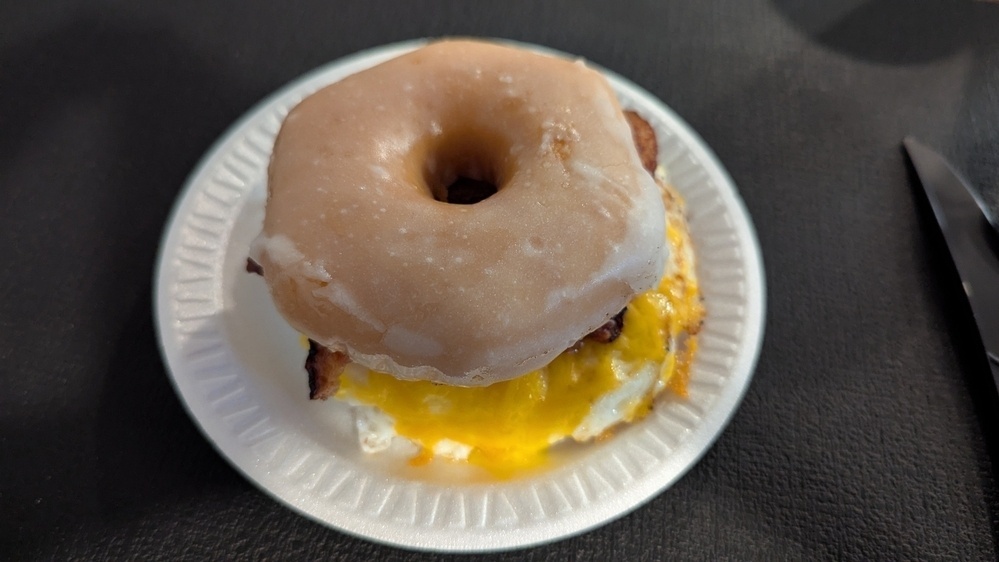 A glazed donut sandwich filled with a fried egg and melted cheese is placed on a white plate.