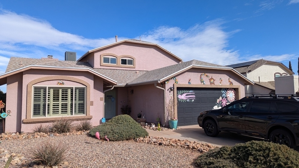 A suburban house with decorative elements on the garage door and a black car parked in the driveway, set under a blue sky.