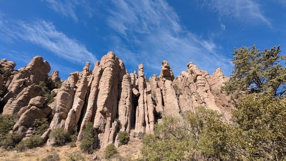 Towering rock formations rise against a blue sky with scattered clouds, surrounded by sparse vegetation.