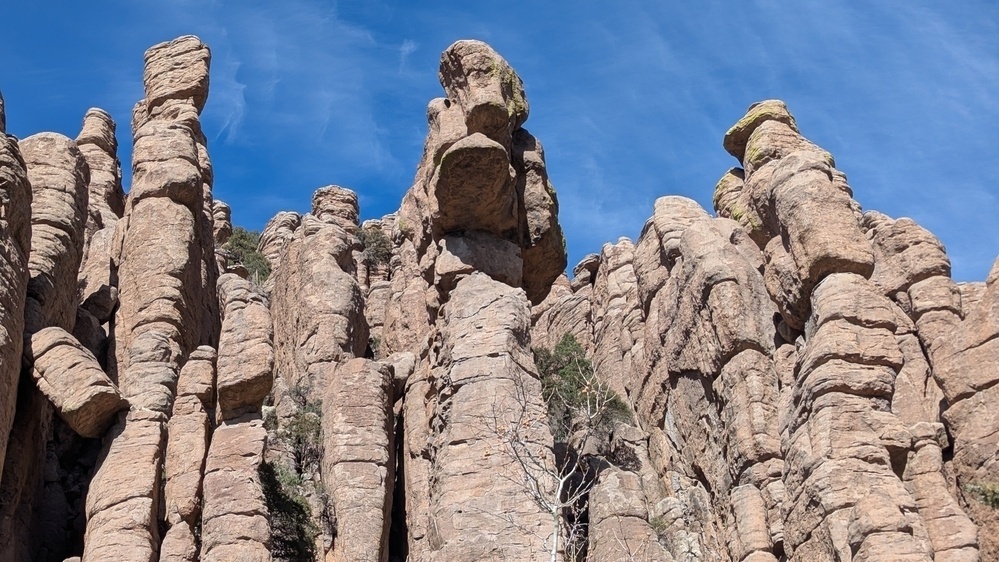 Rock formations tower against a clear blue sky, with various shapes and sizes creating a rugged and dramatic landscape.