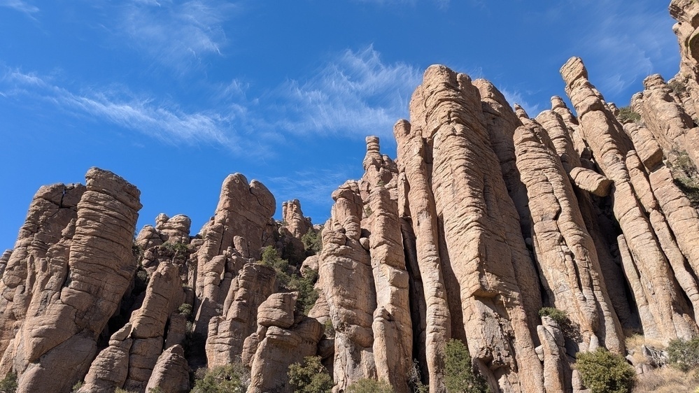 Towering rock formations rise against a backdrop of a clear blue sky with wispy clouds.