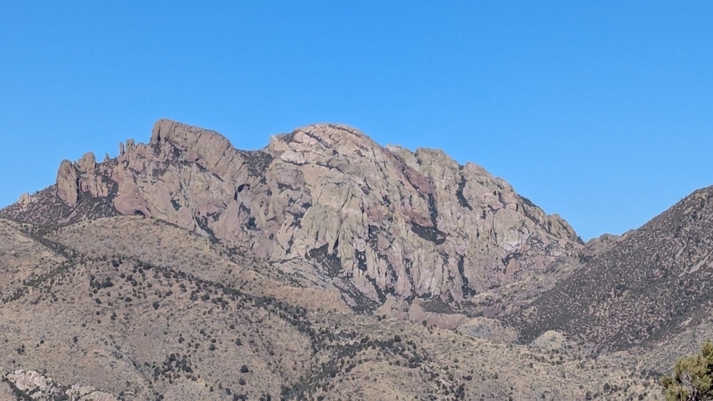 A rocky mountain range with irregular formations is set against a clear blue sky.