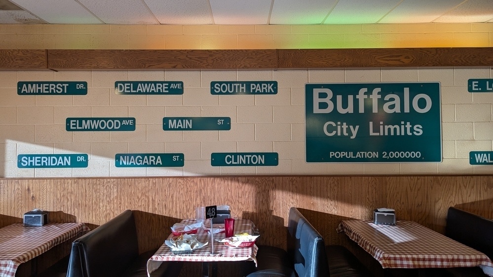 A restaurant interior displays various street sign replicas on the wall with a Buffalo City Limits sign above a booth seating area.